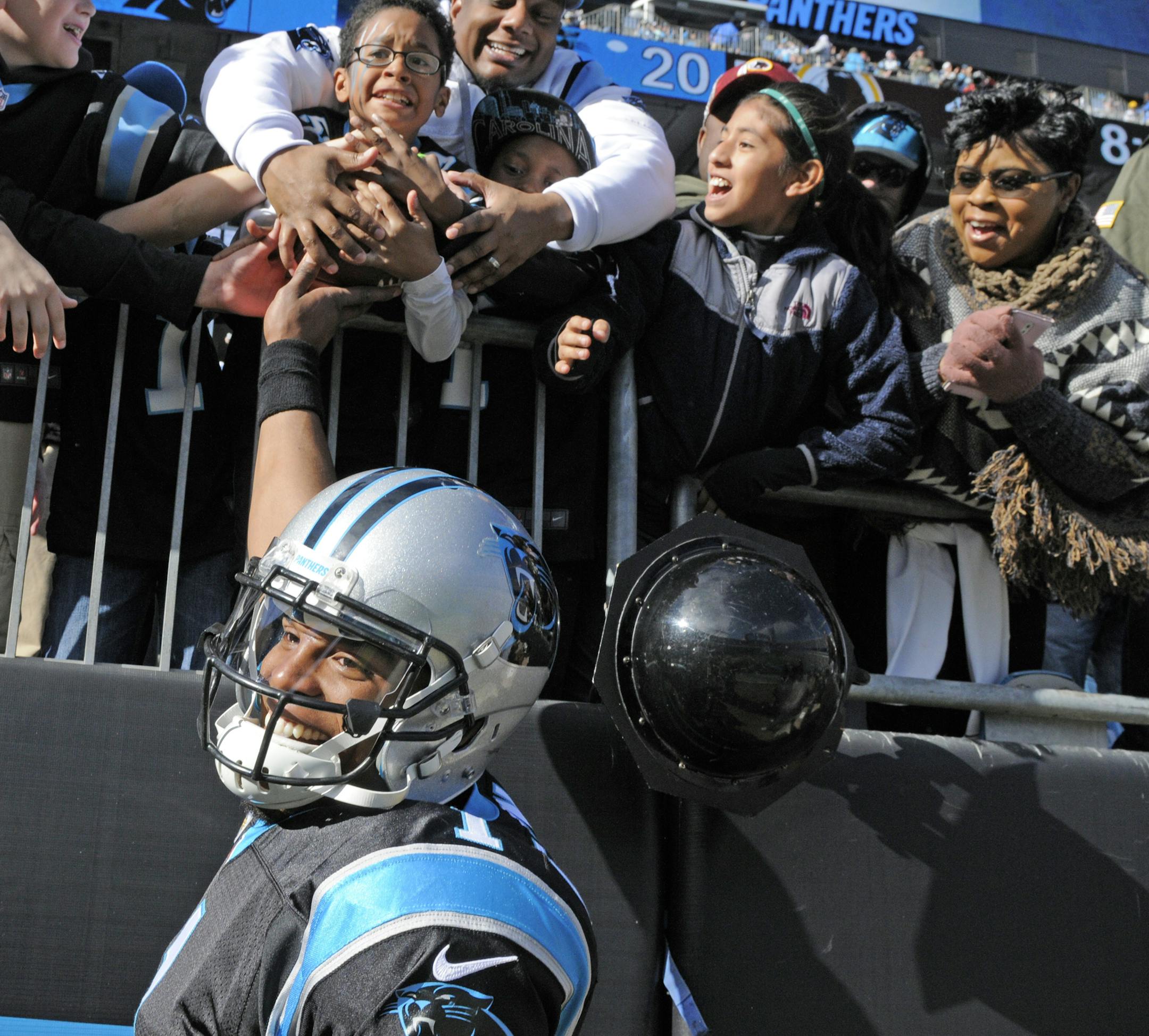 Carolina Panthers' Cam Newton, bottom, hands a touchdown ball to a fan in the first half of an NFL football game against the Washington Redskins in Charlotte, N.C., Sunday, Nov. 22, 2015. (AP Photo/Mike McCarn)