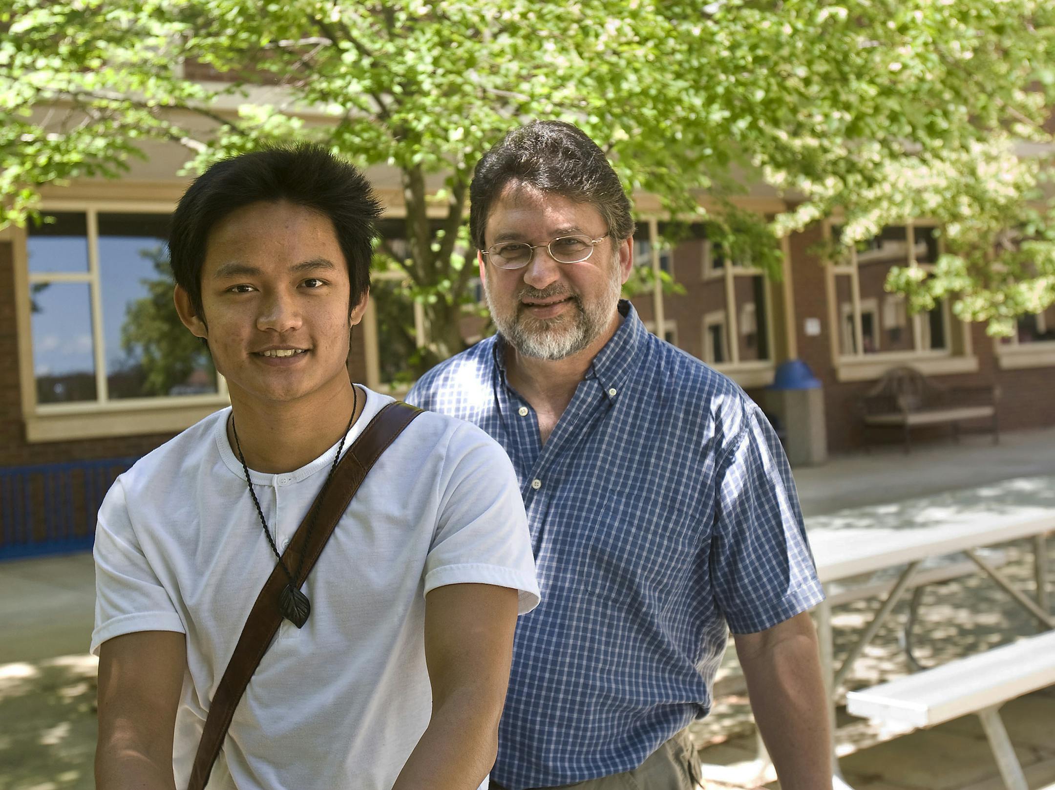 ADVANCE FOR THE WEEKEND OF JULY 19-20 AND THEREAFTER - In a July 3, 2014 photo, Chung Eang Lip and Pastor Nick Ficher-Broin sit in front of the Rochester Community and Technical College entrance in Rochester, Minn, where Lip is a student. Lip was orphaned at 14 but always dreamed of being part of a family. The Cambodian youth had his hopes come true when he met Ficher-Broin and his wife Cindy of Rochester, Minn. Lip (AP Photo/Rochester Post-Bulletin, Jerry Olson.)