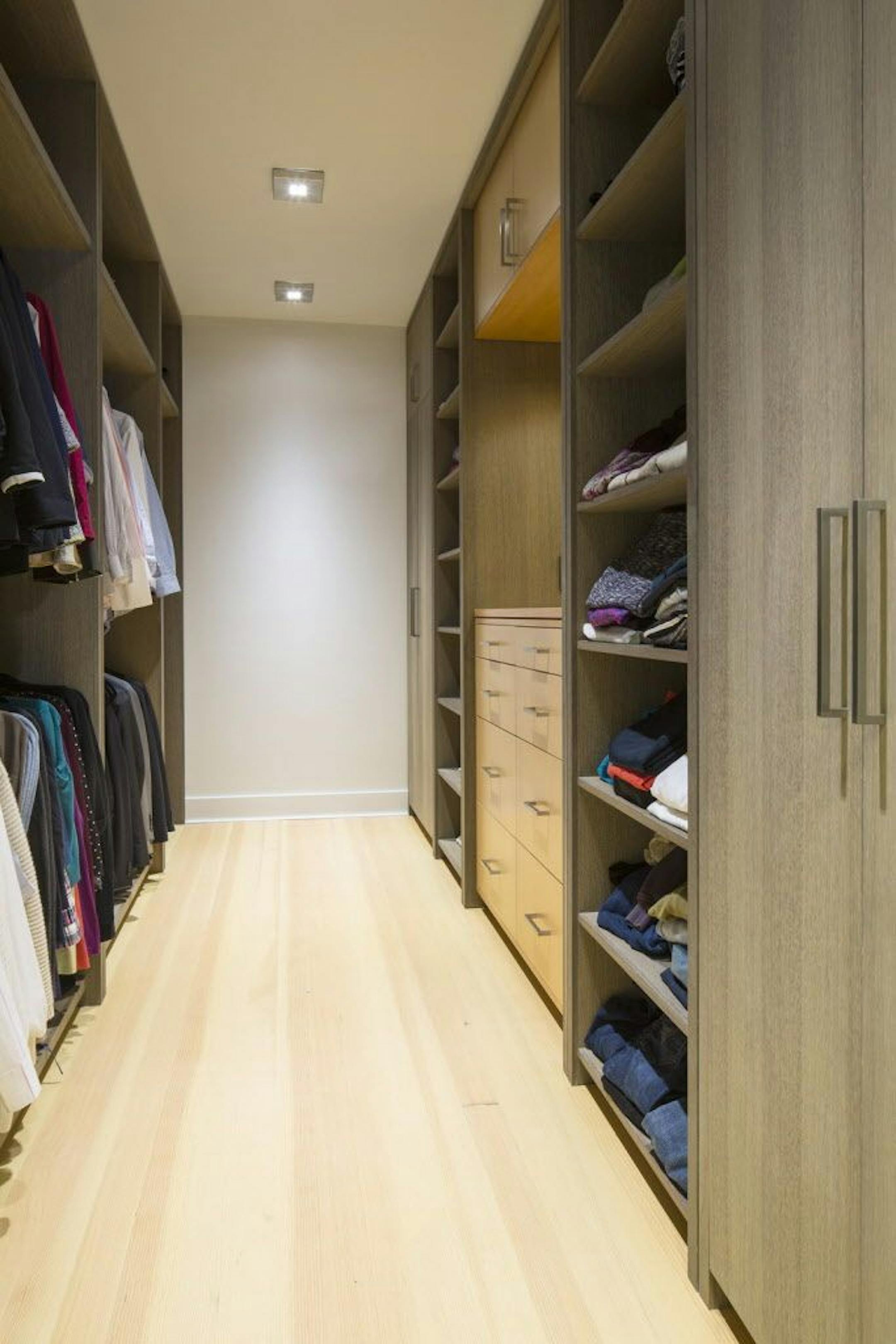 The spacious walk-in closet has sections for hanging clothes, built-in drawers, lots of shelves and a mirror.