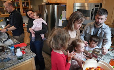Sean Boley washes dishes as Betsy Ohrn holds daughter Esme, 1, while spouse Tye Schulke and their son Axel, 3, help Sara Kemper and daughters Ivy, 4, 