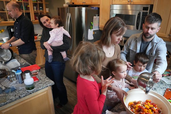 Sean Boley washes dishes as Betsy Ohrn holds her daughter Esme, 1, while her spouse Tye Schulke and their son Axel, 3, help Sara Kemper and her daught