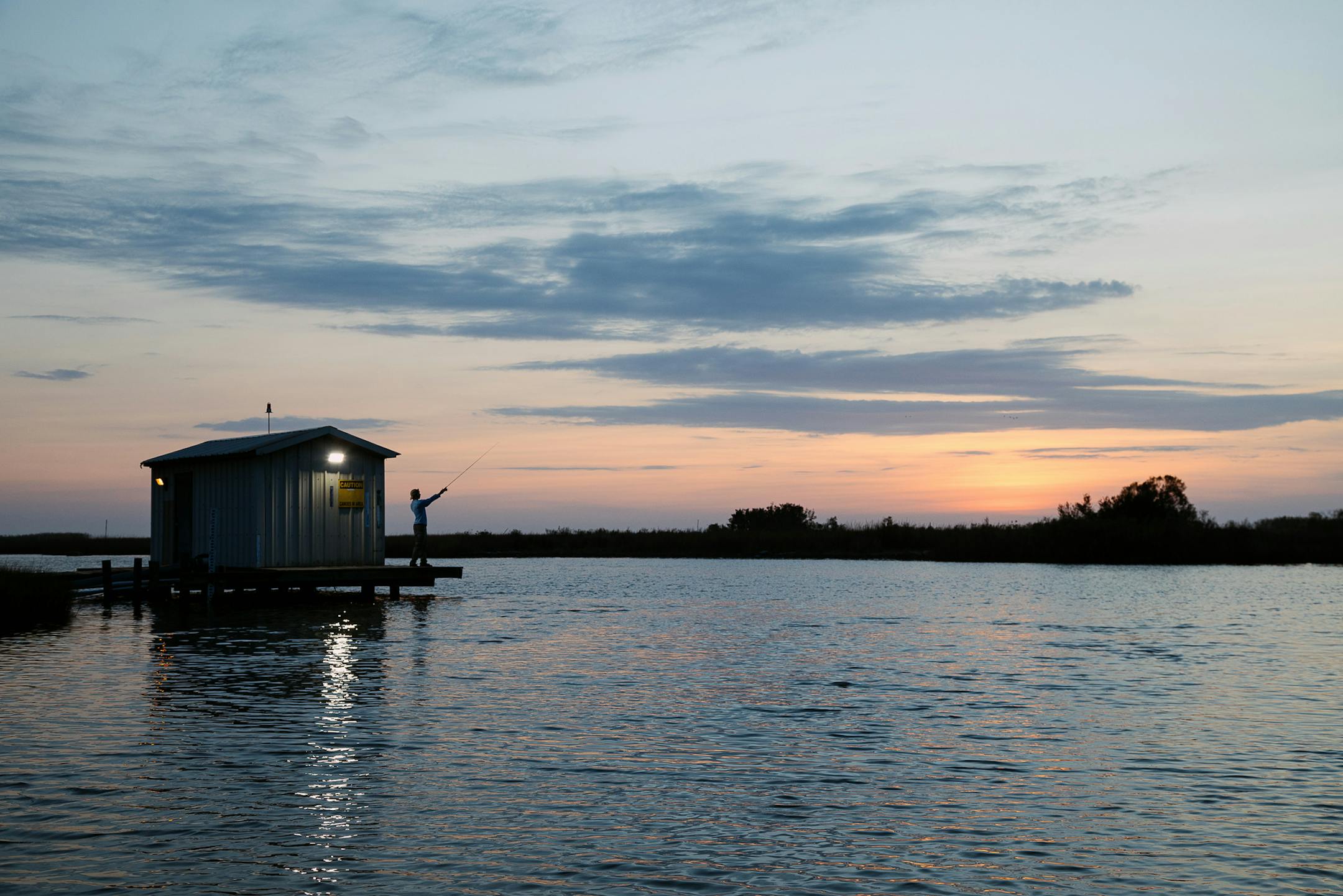 A lab technician fishes off the dock at the Louisiana Universities Marine Consortium facility in Cocodrie, La., on Dec. 9, 2019. Around the country, from New Jersey to Massachusetts, Virginia to Oregon, education centers and marine laboratories like this one are bracing against rising seas and a changing climate. (Bryan Tarnowski/The New York Times)