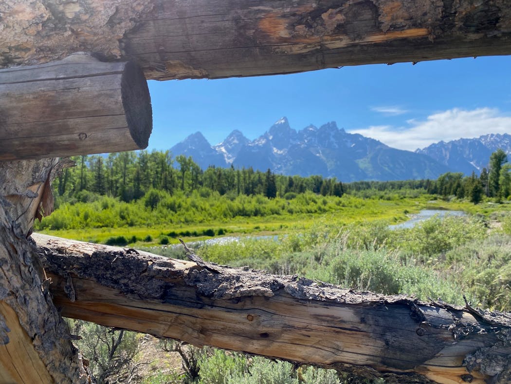The 13,771-foot Grand Teton and the nascent Snake River through the frame of a split-rail fence.