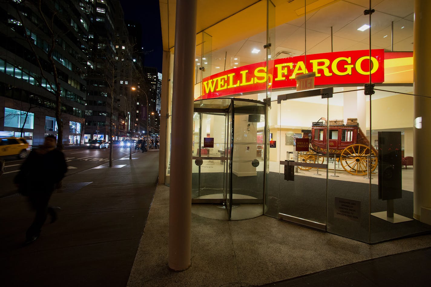 Pedestrians pass in front of a Wells Fargo & Co. bank branch at night in New York, U.S., on Monday, April 7, 2014. Wells Fargo & Co. is expected to release earnings figures on April 11. Photographer: Craig Warga/Bloomberg