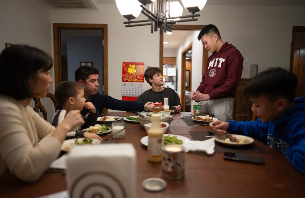 Sunnie He and David Krieger and her son, Theo, left, gathered for dinner with their three international students, Quang Do, his brother Quan Do, standing, and Matvii Suminov, from right, in their on-campus apartment in Mendota Heights. 