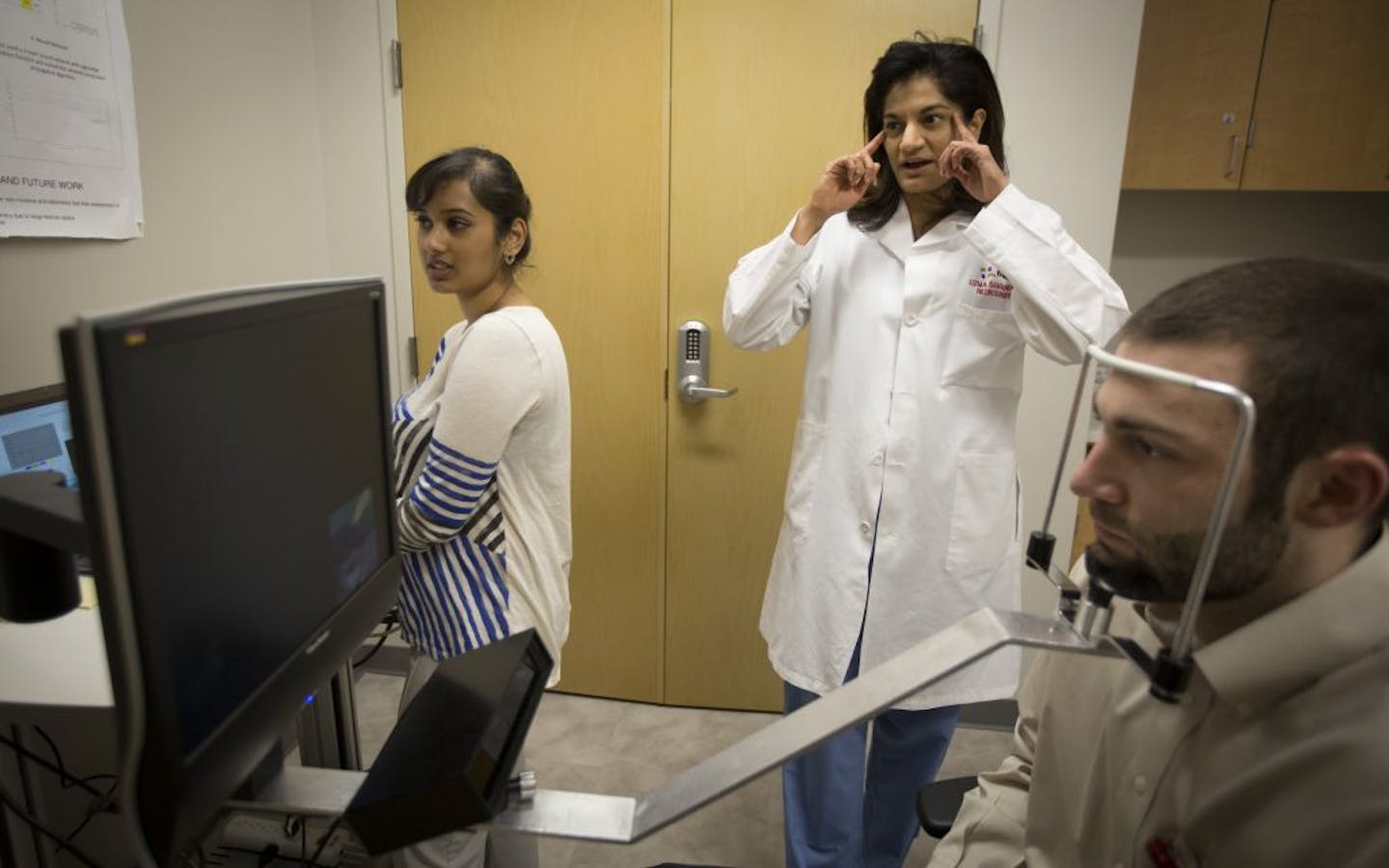 Dr. Uzma Samadani, middle, talked about eye movements as research assistant Sam Daly, in front, sat through a test conducted by Vikalpa Dammavalam, left, at HCMC meant to help study concussion injuries.