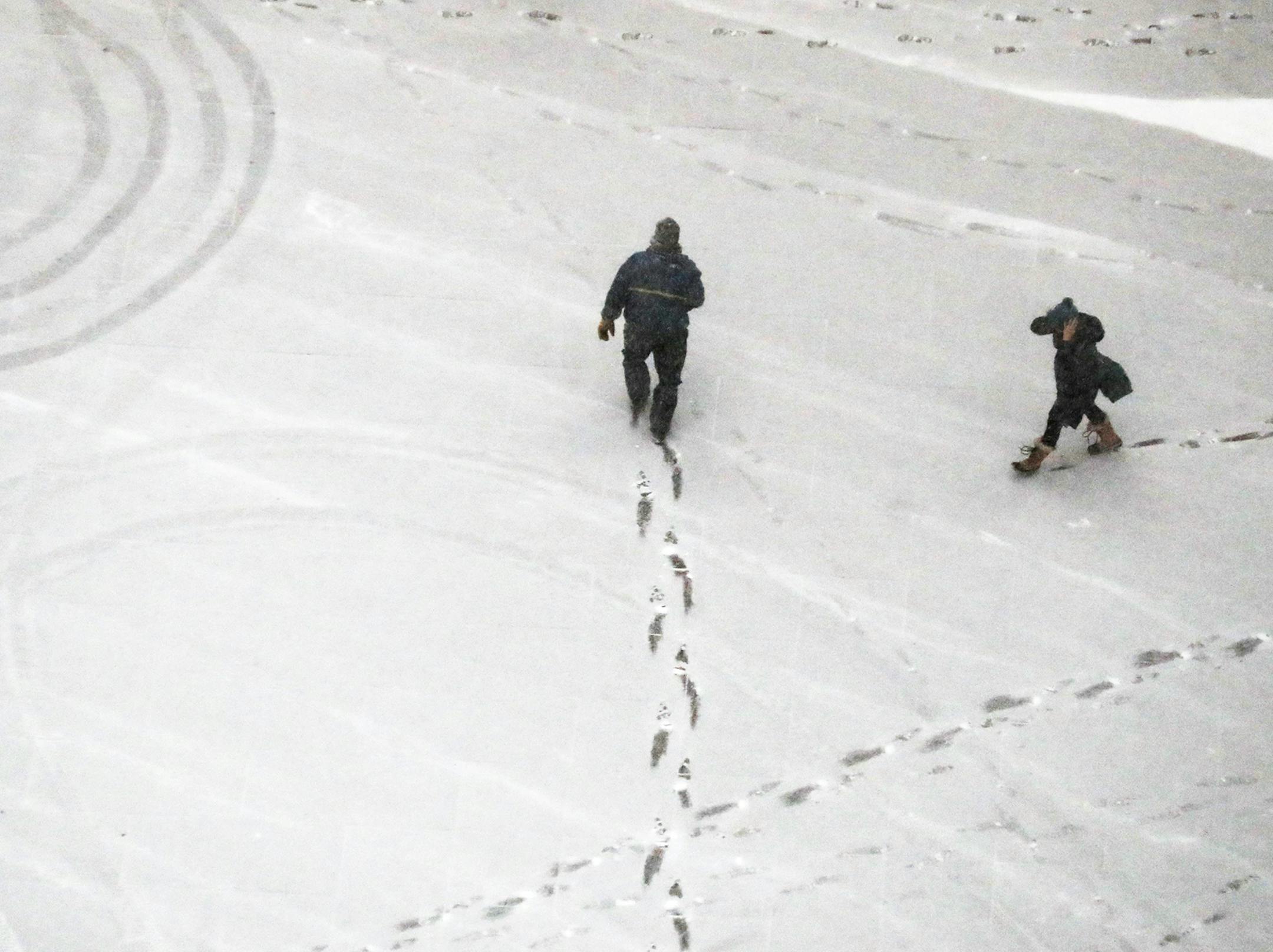Pedestrians leave foot prints behind while navigating fresh snow near the US Bank Plaza Thursday.