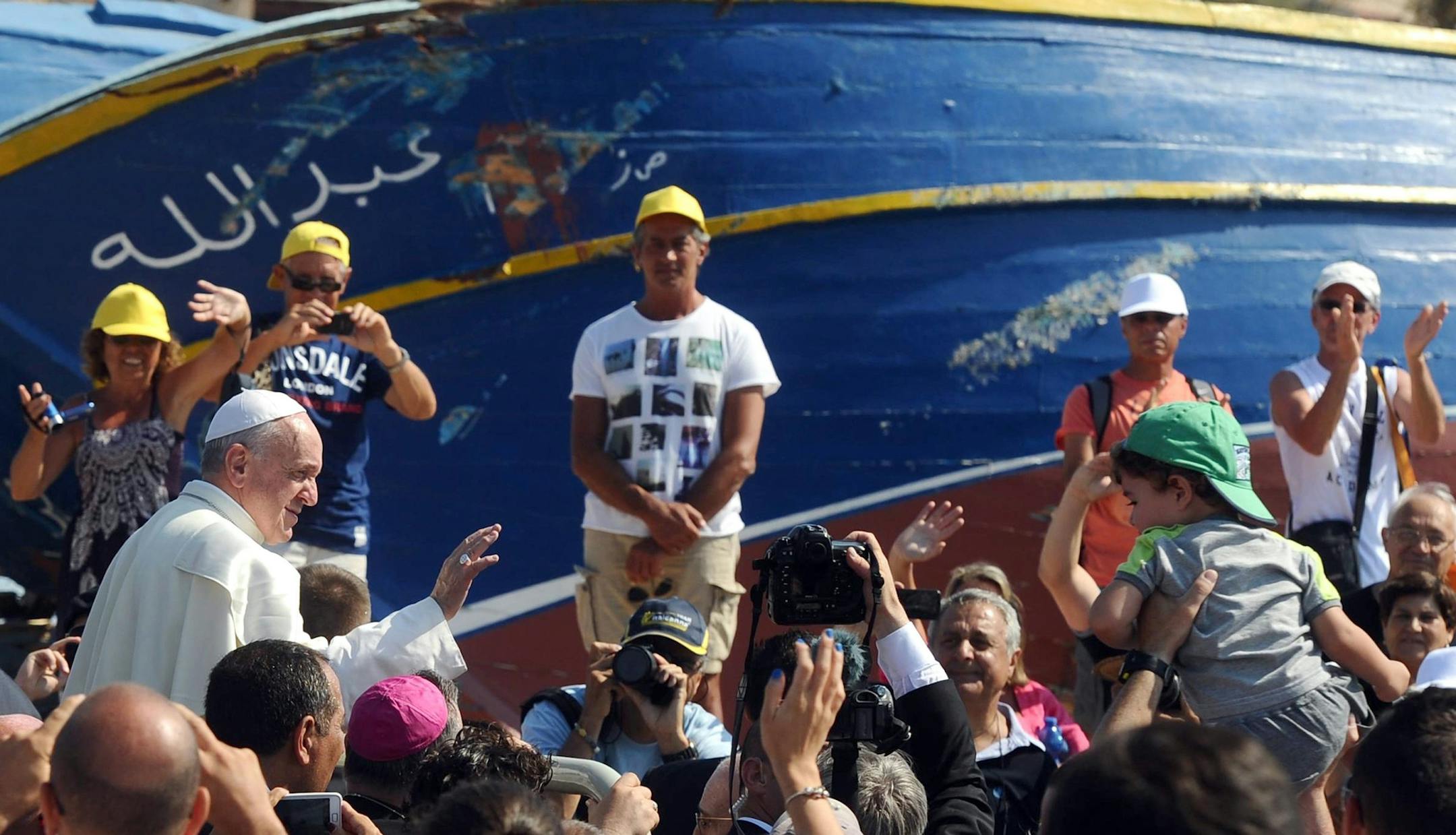 With a beached ship behind him, Pope Francis blesses the faithful during his visit to Lampedusa Island in Italy on July 8, 2013, one of the many points of entry into Europe that has drawn many migrants from North Africa.