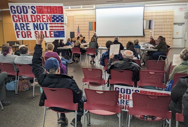 A man attending the Great River Regional Library board meeting Tuesday, Nov. 21, holds a sign while Avon resident Sandy Klocker speaks at the open for