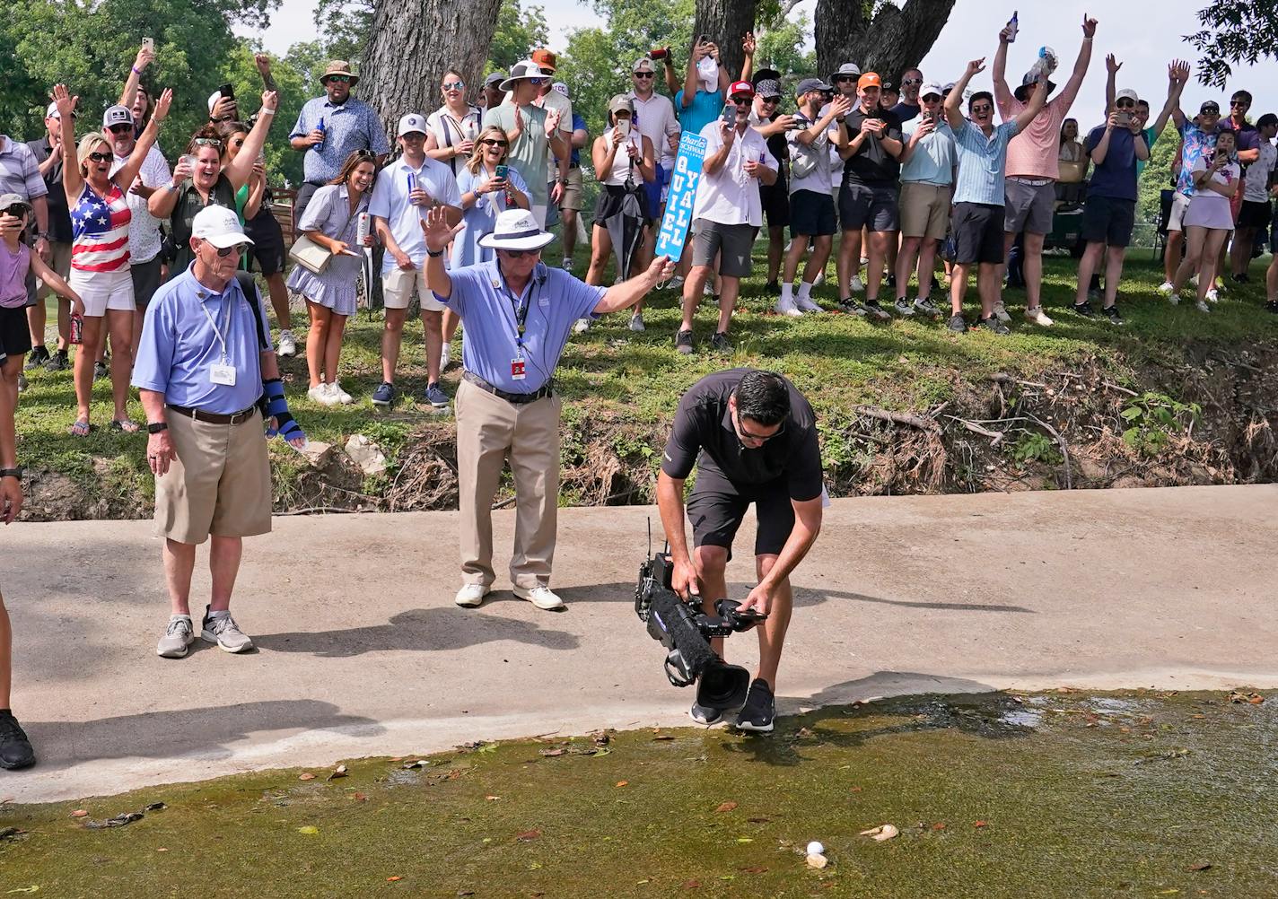 A cameraman films and the gallery cheers as Emiliano Grillo's ball comes to a rest against a rock after floating down a concrete drainage canal on the 18th hole during the final round of the Charles Schwab Challenge golf tournament at Colonial Country Club in Fort Worth, Texas, Sunday, May 28, 2023. (AP Photo/LM Otero)