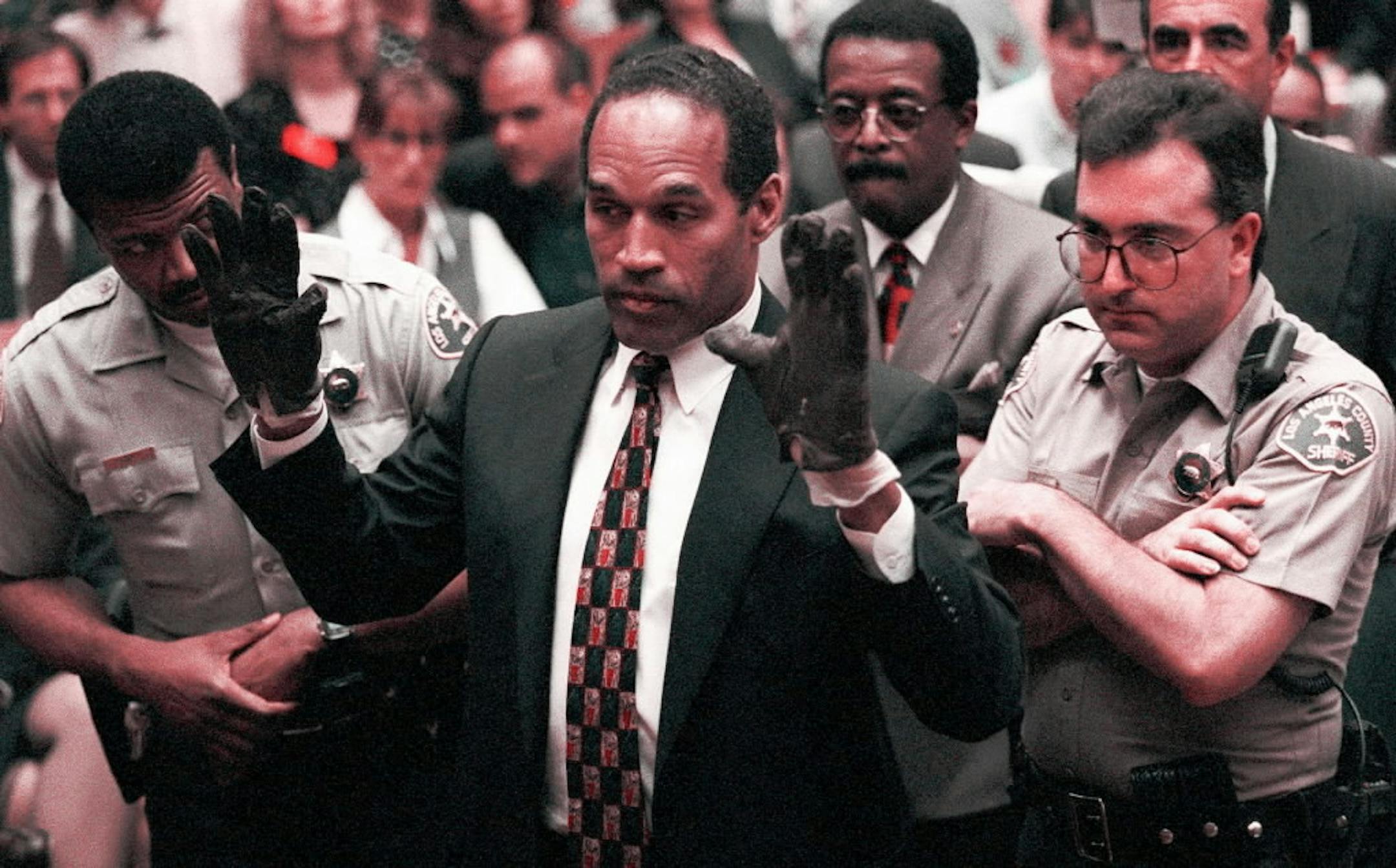 O.J. Simpson holds his hands up to the jury during testimony in Los Angeles Thursday, June 15, 1995, to show the bloody gloves the prosecution says he wore when he murdered Nicole Brown Simpson and Ron Goldman. Simpson put the gloves on at the request of the prosecution, who accused him of faking a struggle to pull them on. In the background are defense attorneys Johnnie Cochran Jr., third from right and Robert Shapiro, right.
