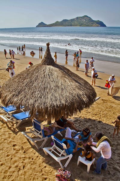 Vacationers relax under a palapa in front of the family-friendly El Cid Castilla Hotel in Mazatlan, Mexico.