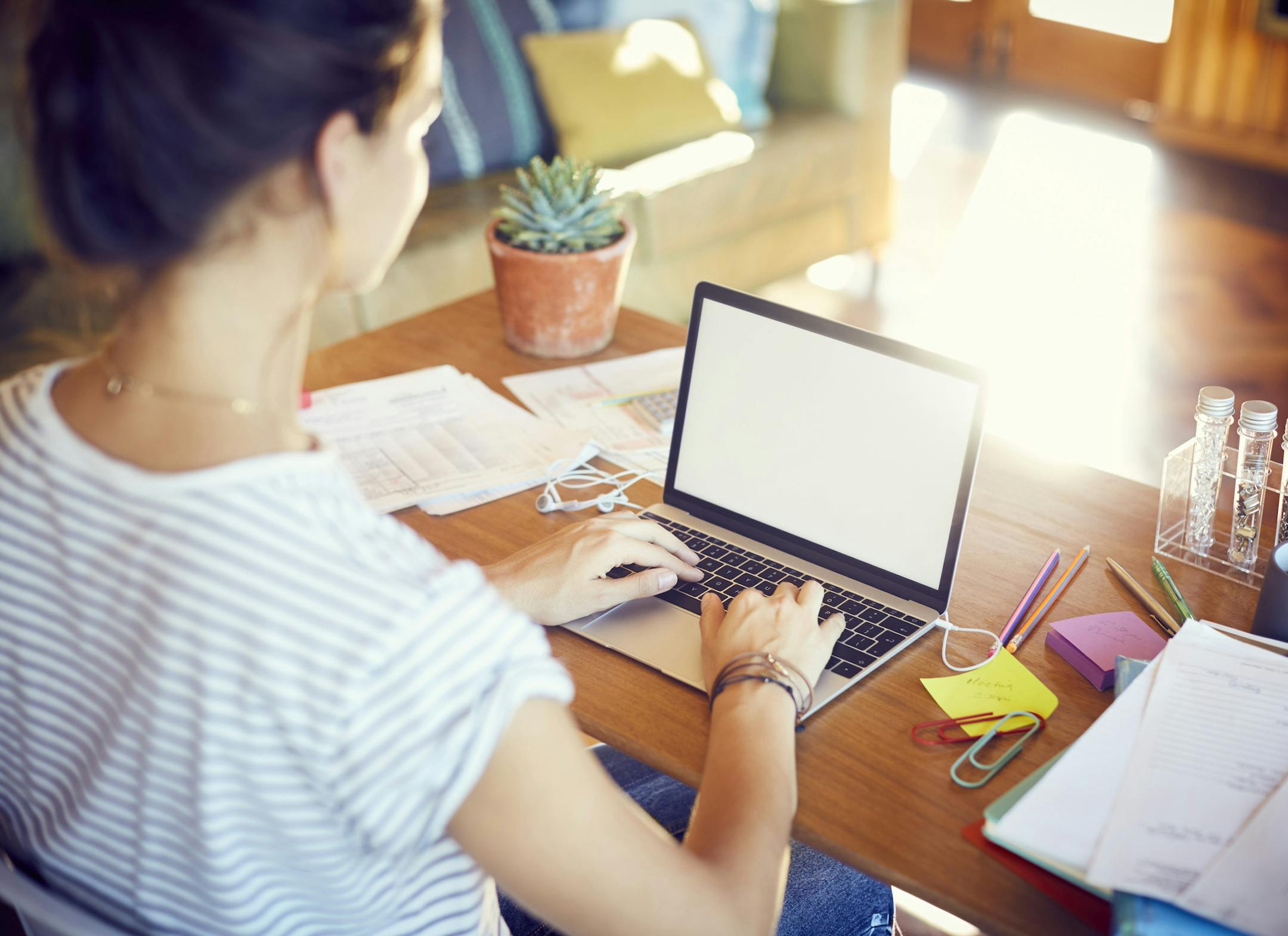High angle view of woman is working at table. Over the shoulder view of female using laptop. Selective focus is on technology with blank screen.