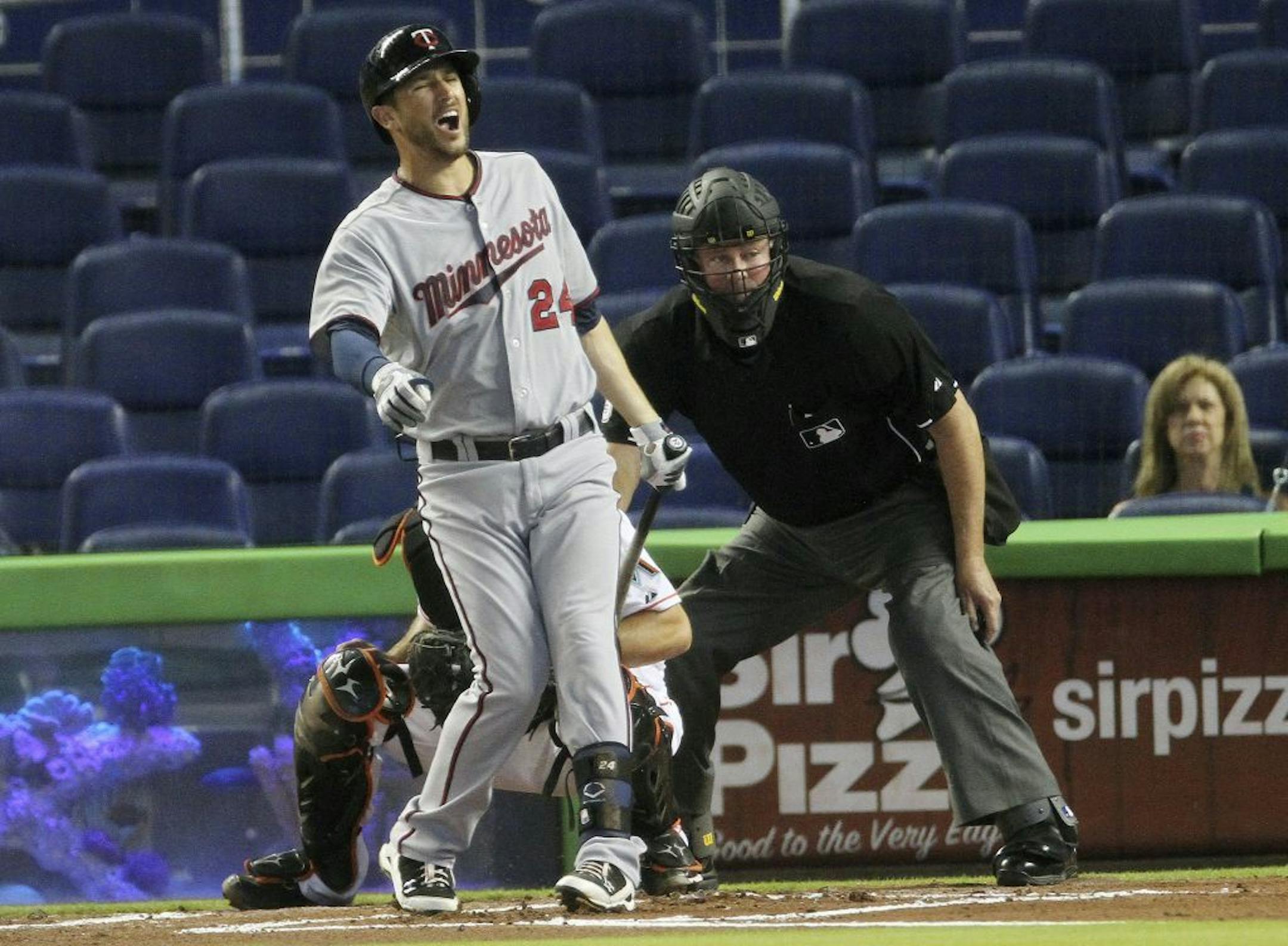 Minnesota Twins batter Trevor Plouffe (24) reacts after getting hit with a foul ball he hit in the first inning of a baseball game against the Miami Marlins in Miami. Behind Plouffe are Marlins catcher Jeff Mathis and home plate umpire Tim Welks.