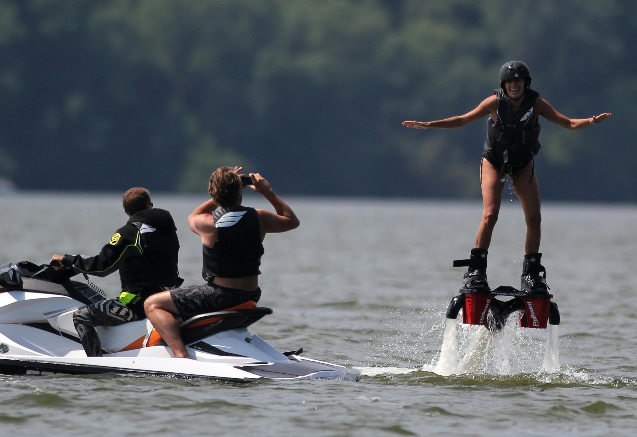 Holly Matzke (right) takes flyboarding lessons from Rodney Jansen (left) while Tom Garneau (center) takes pictures, on Friday afternoon at Lake Waconia.] Rodney Jansen gave flyboarding lessons on Lake Waconia on Friday afternoon. Jansen started flyboarding three years ago, and started his rental company two years ago. His last weeks of summer will be busy as he is booked through the end of the season. MONICA HERNDON Waconia, MN 08/15/14
