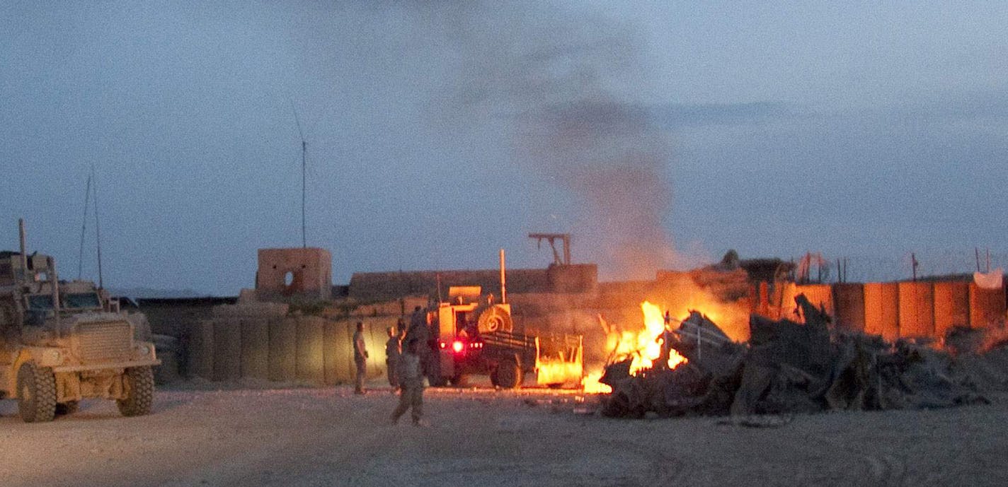 In this April 28, 2011 photo, an Afghan National Army pickup truck passes parked U.S. armored military vehicles, as smoke rises from a fire in a trash burn pit at Forward Operating Base Caferetta Nawzad, Helmand province south of Kabul, Afghanistan. U.S. Marines recently pacified this once violent town center, but there isn't much left of it. Nawzad's center is quiet, but its desert outskirts are still contested. The southwest province of Helmand, where Nawzad sits, is where the Afghan war is be