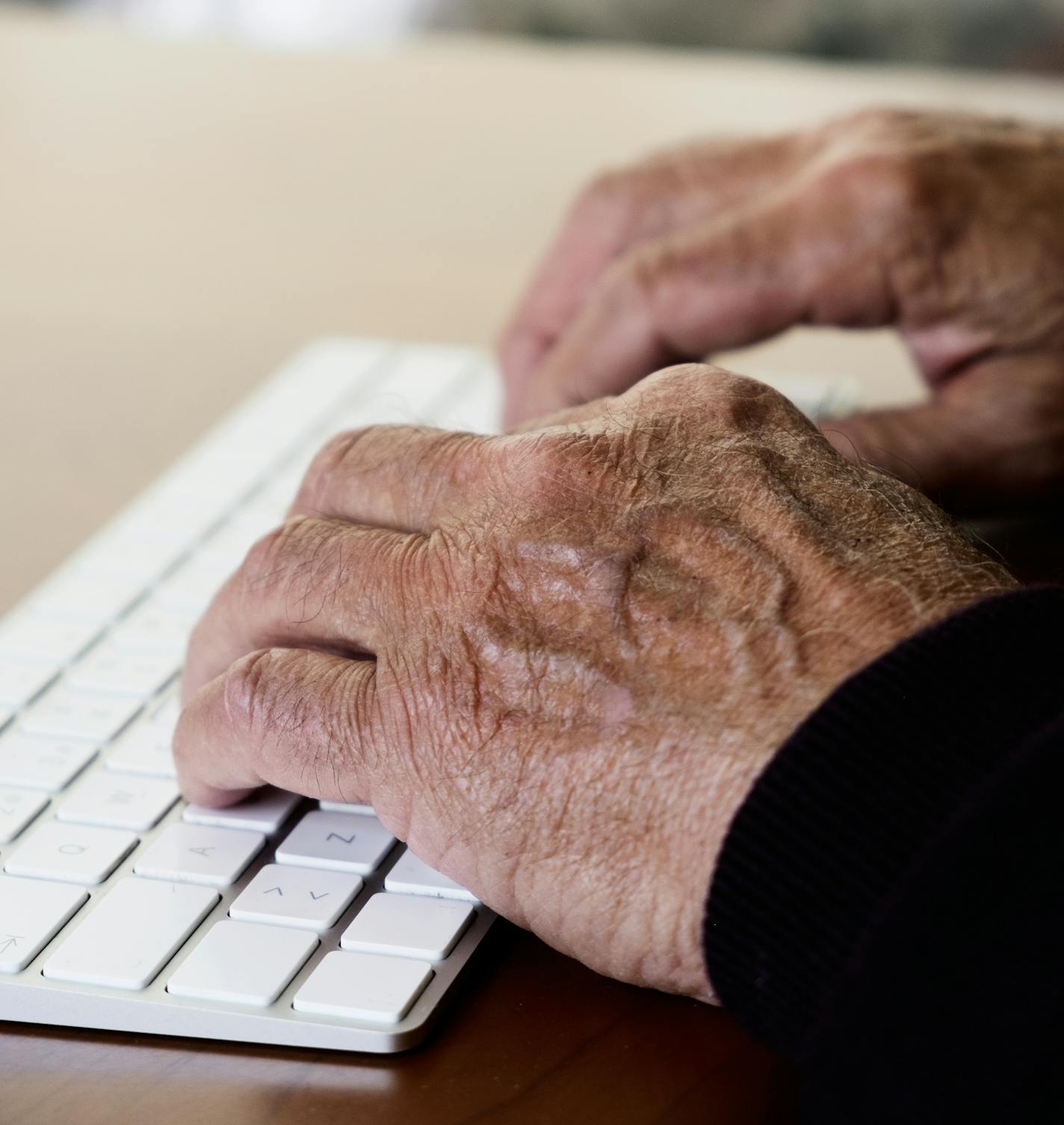 closeup of an old caucasian man sitting at an elegant wooden table typing in a keyboard