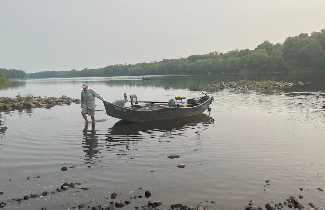 On a fishing day when smoke from Canadian wildfires clouded the sky, John Butler of Marine on St. Croix pulls a drift boat to a St. Croix River shoreline. 
