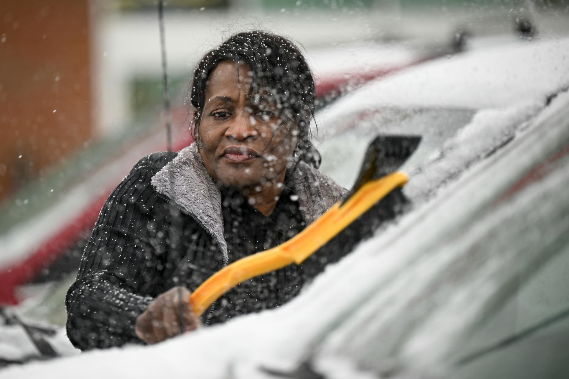 Becky Aburime, of Little Canada, brushes off her truck's windshield after grocery shopping Tuesday, outside Hy-Vee in Robbinsdale. "I love it," said Aburime of the coming snow storm. "It's cozy and you can warm up with your family at home."