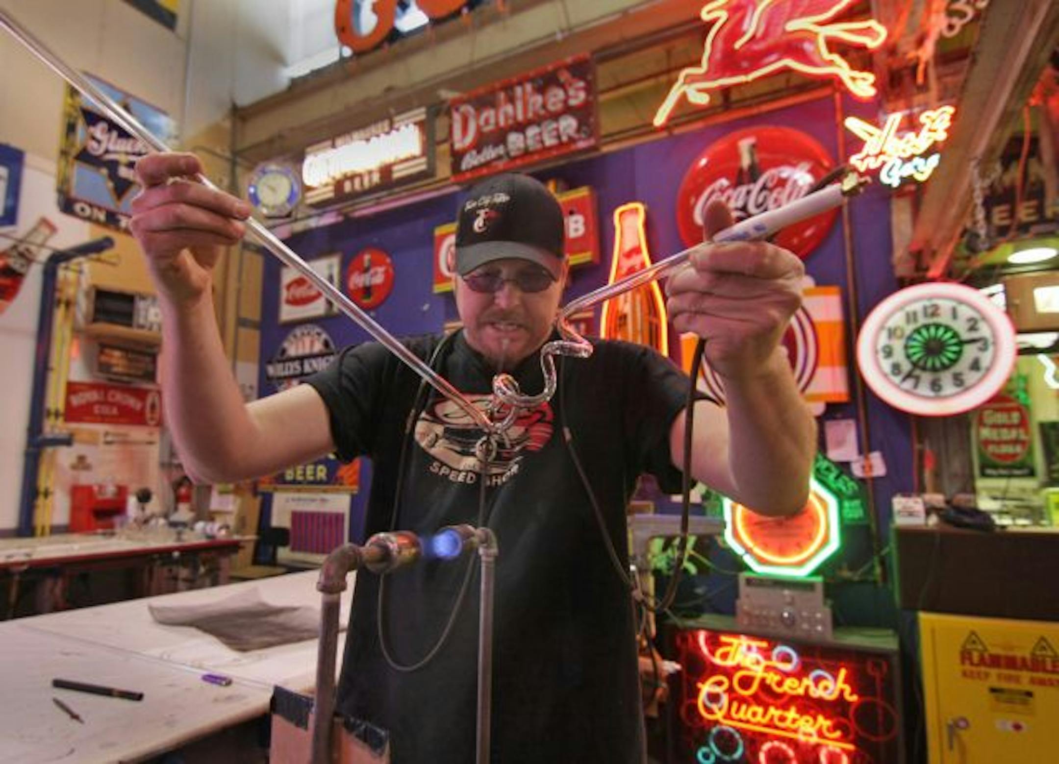 Matt Thompson, of Skyline Neon bends and shapes a glass tube using a gas flame for heat, and blowing into the tube through a tube/hose so that it retains its cylindrical shape during the process.