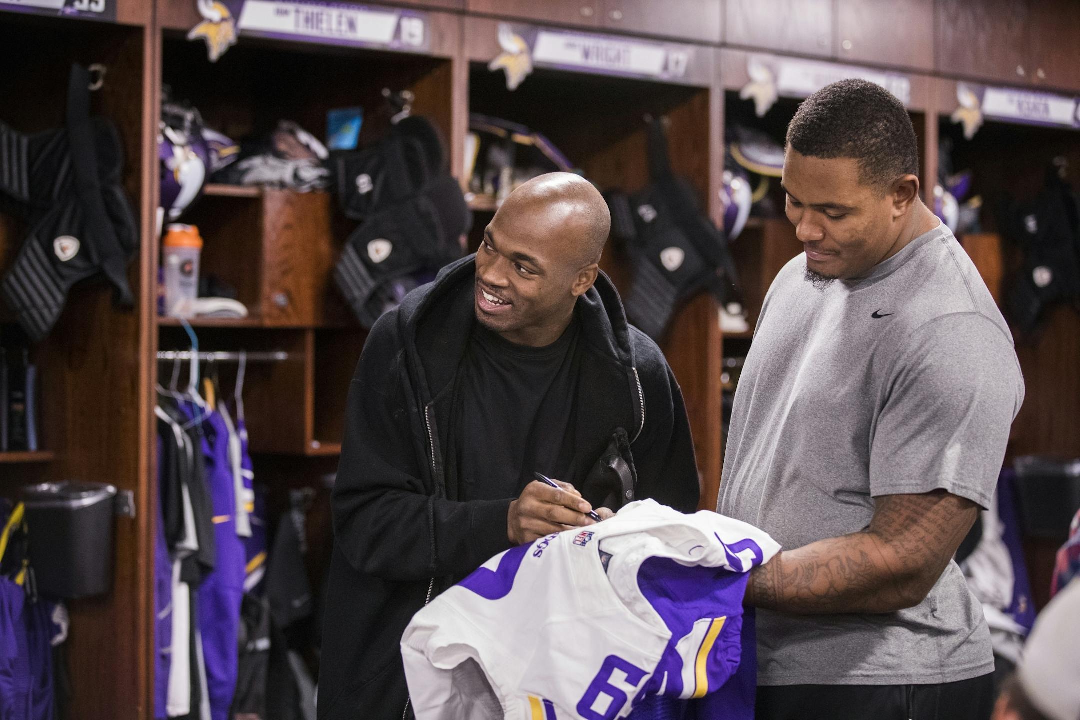 Adrian Peterson, left, signs a jersey for teammate Rashod Hill.