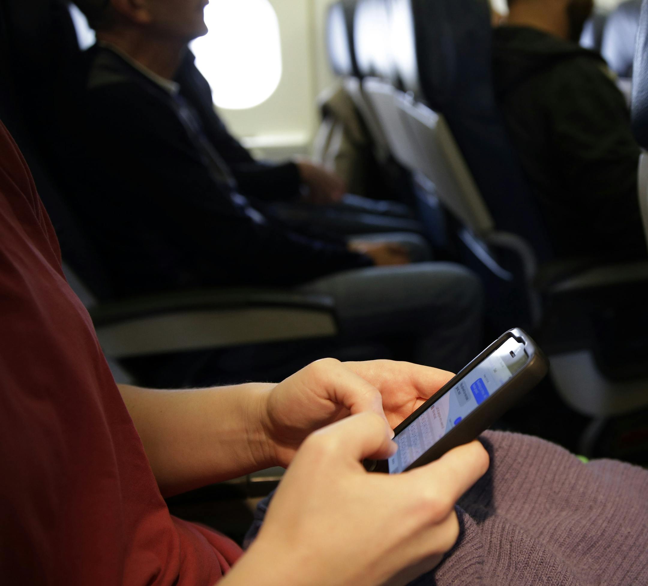 FILE - This Oct. 31, 2013 file photo shows a plane passenger checking her cell phone before a flight in Boston. While one government agency considers allowing cellphone calls on passenger planes, another now wants to ban them. The Transportation Department signals that it wants to impose a ban on inflight cellphone calls, just two months after the Federal Communications Commission (FCC) voted to pursue lifting the current ban. The FCC regulates wireless communications, while the transportation d