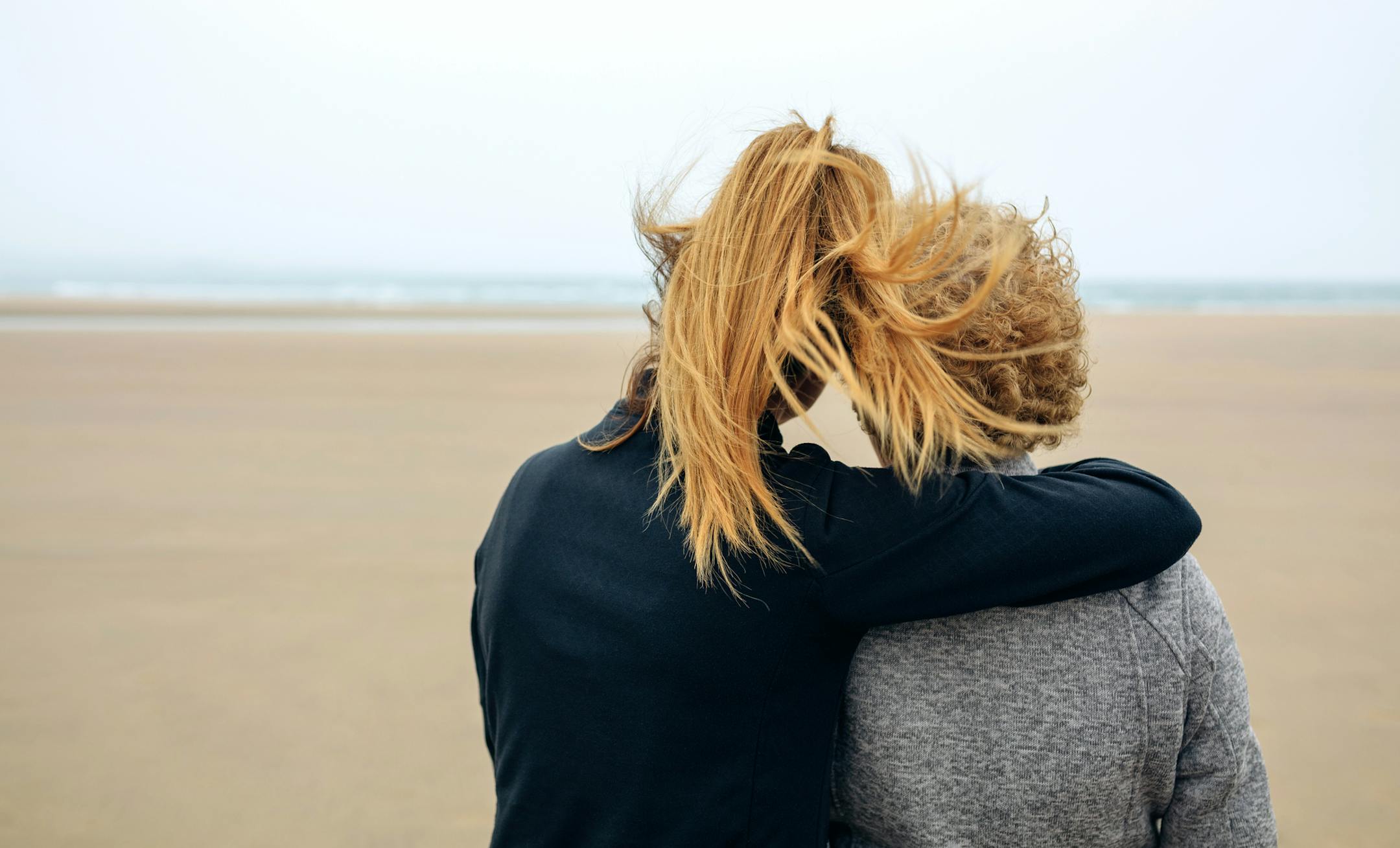 Back view of senior and young woman looking at sea on the beach in autumn
