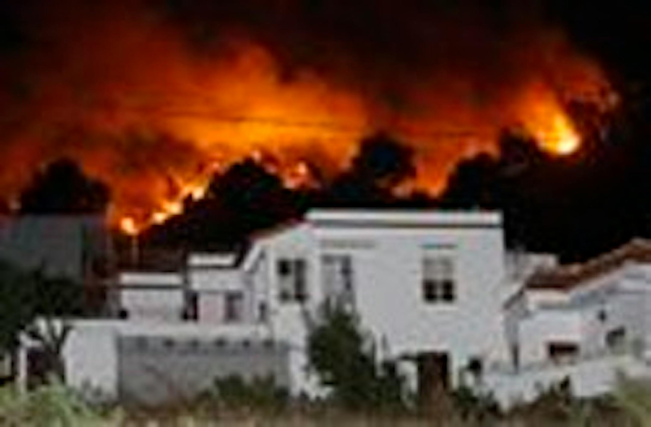 In this photo taken Saturday, Aug. 1, 2009, flames from a forest fire are seen behind a house in Fuencaliente on the Canary Island of La Palma, Spain. A forest fire fanned by high winds has forced the evacuation of about 4,000 residents on the Canary Island of La Palma, the Spanish government said Saturday. (AP Photo/Carlos Moreno)