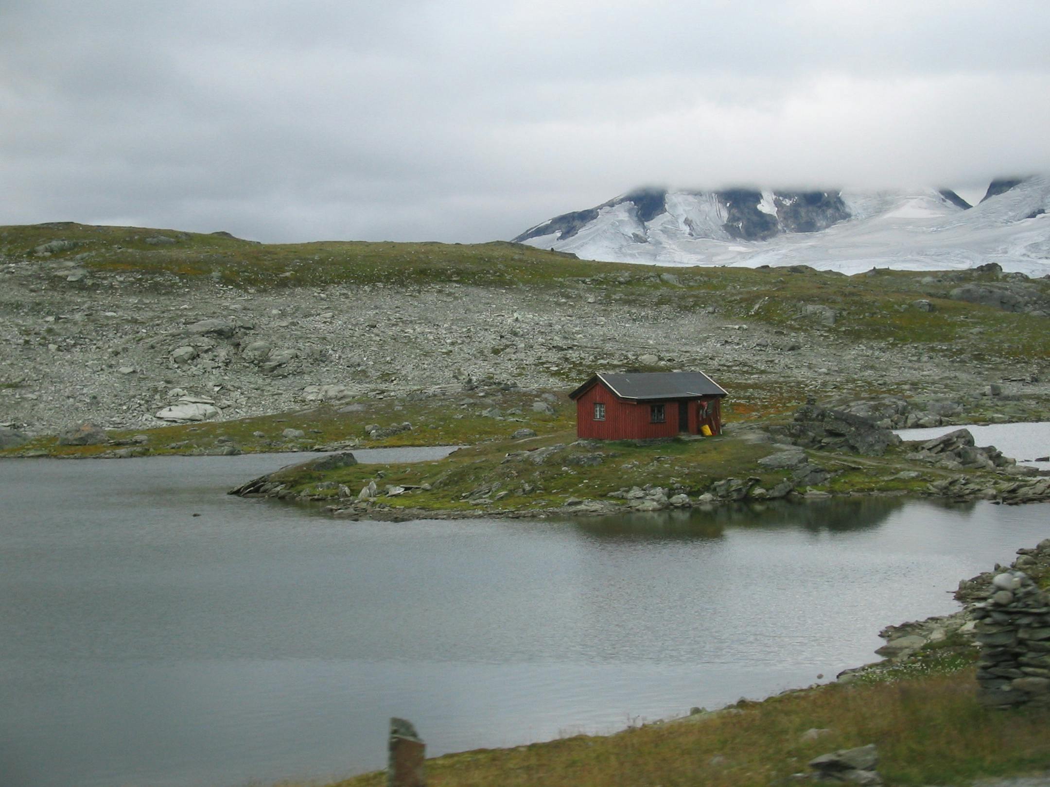 This lonely cabin ringed by a glacier-fed lake occupies a classic Norwegian landscape made up of calm waters, snow-capped mountains, a rocky plateau and a long stretch of rugged, simple beauty.