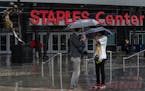 Tourist stand under umbrellas in rain outside Staples Center, home to hockey's Los Angeles Kings and basketball's Los Angeles Lakers, Clippers and Spa