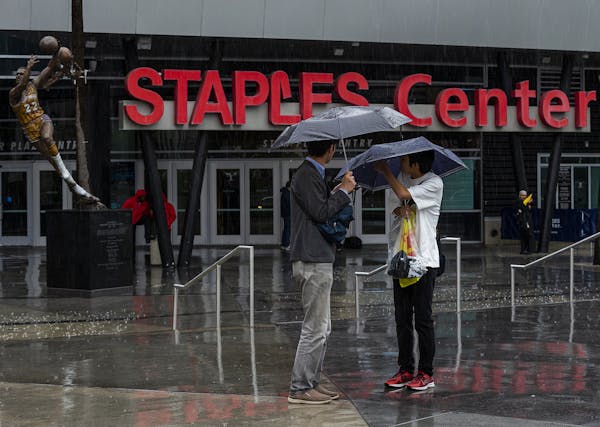 Tourist stand under umbrellas in rain outside Staples Center, home to hockey's Los Angeles Kings and basketball's Los Angeles Lakers, Clippers and Spa
