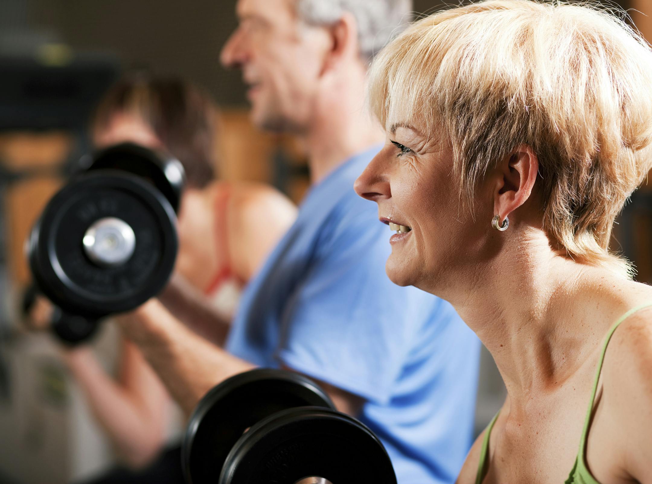 Three senior people - two women and one man - in the gym lifting dumbbells, exercising. istock