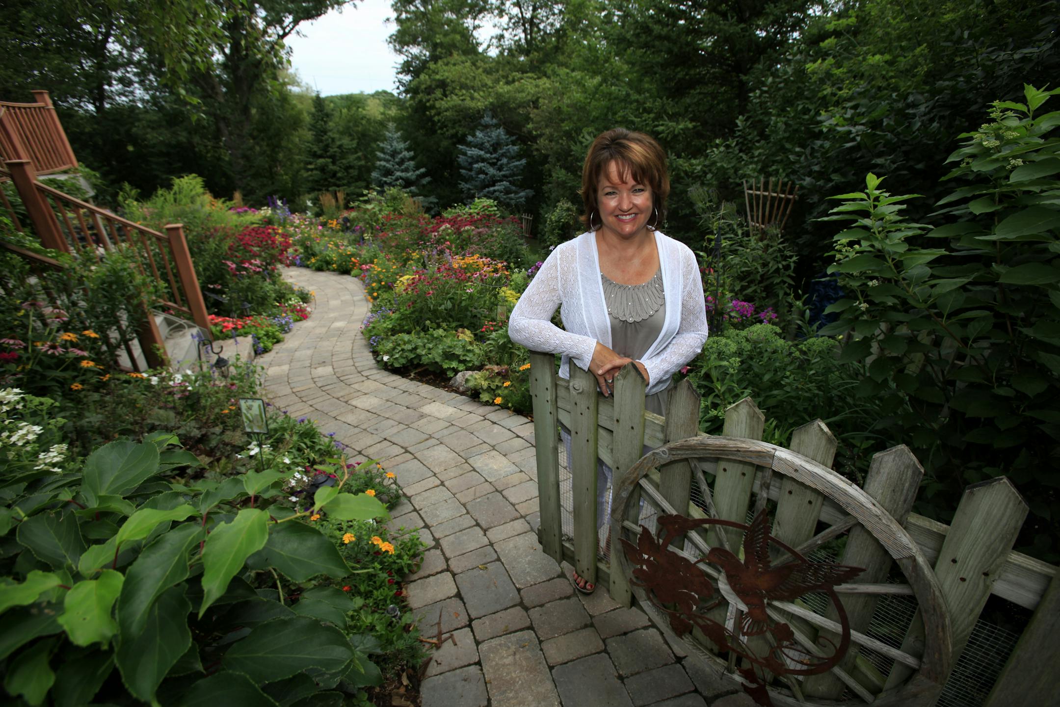 Gardener Jeanne Thatcher at the gate leading to her back-yard garden. She accents with garden art, but sparingly. “I want flowers to be the emphasis,” she said.