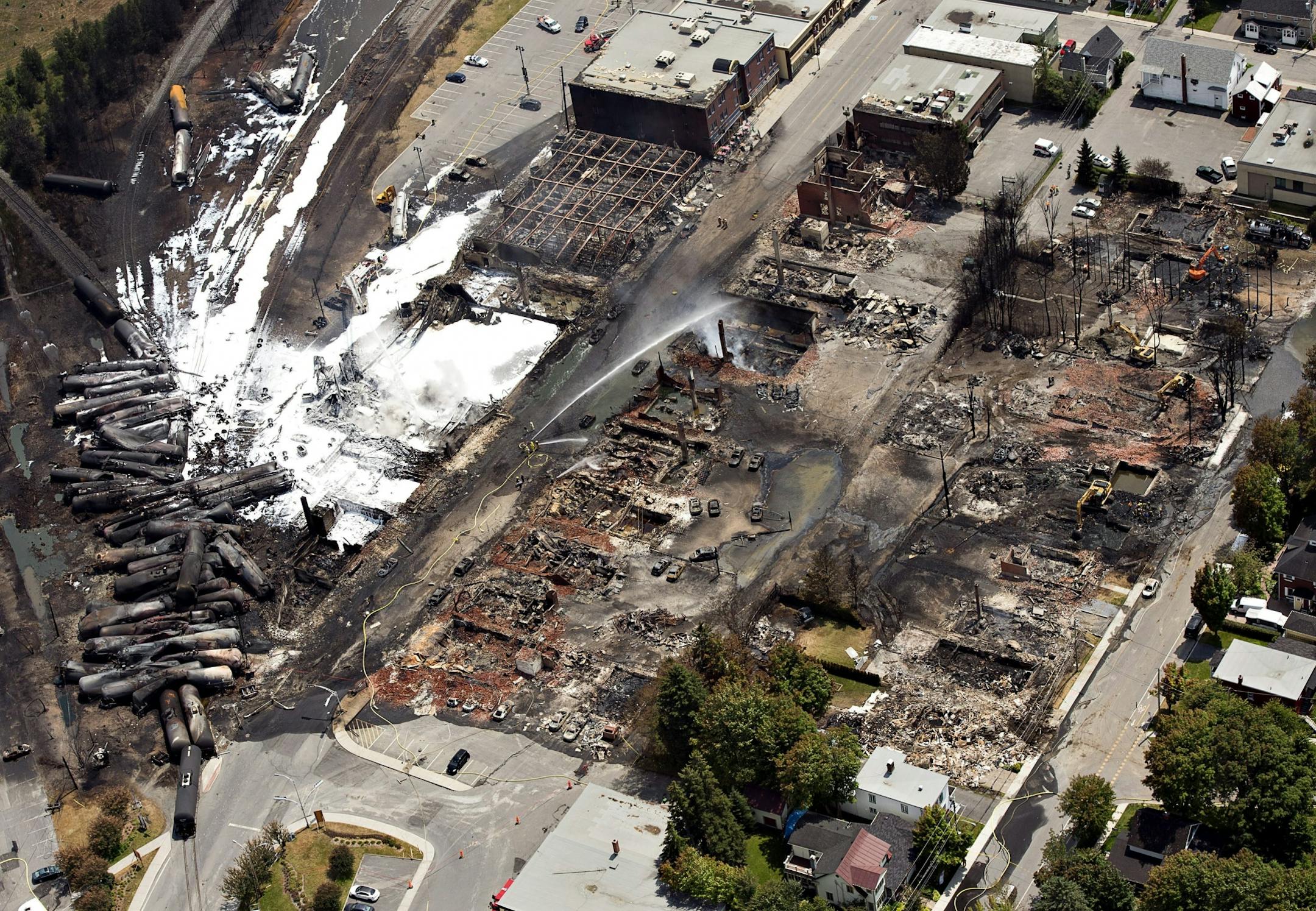 The downtown core lays in ruins as fire fighters continue to water smoldering rubble Sunday, July 7, 2013, in Lac Megantic, Quebec. A runaway train derailed Saturday igniting tanker cars carrying crude oil.