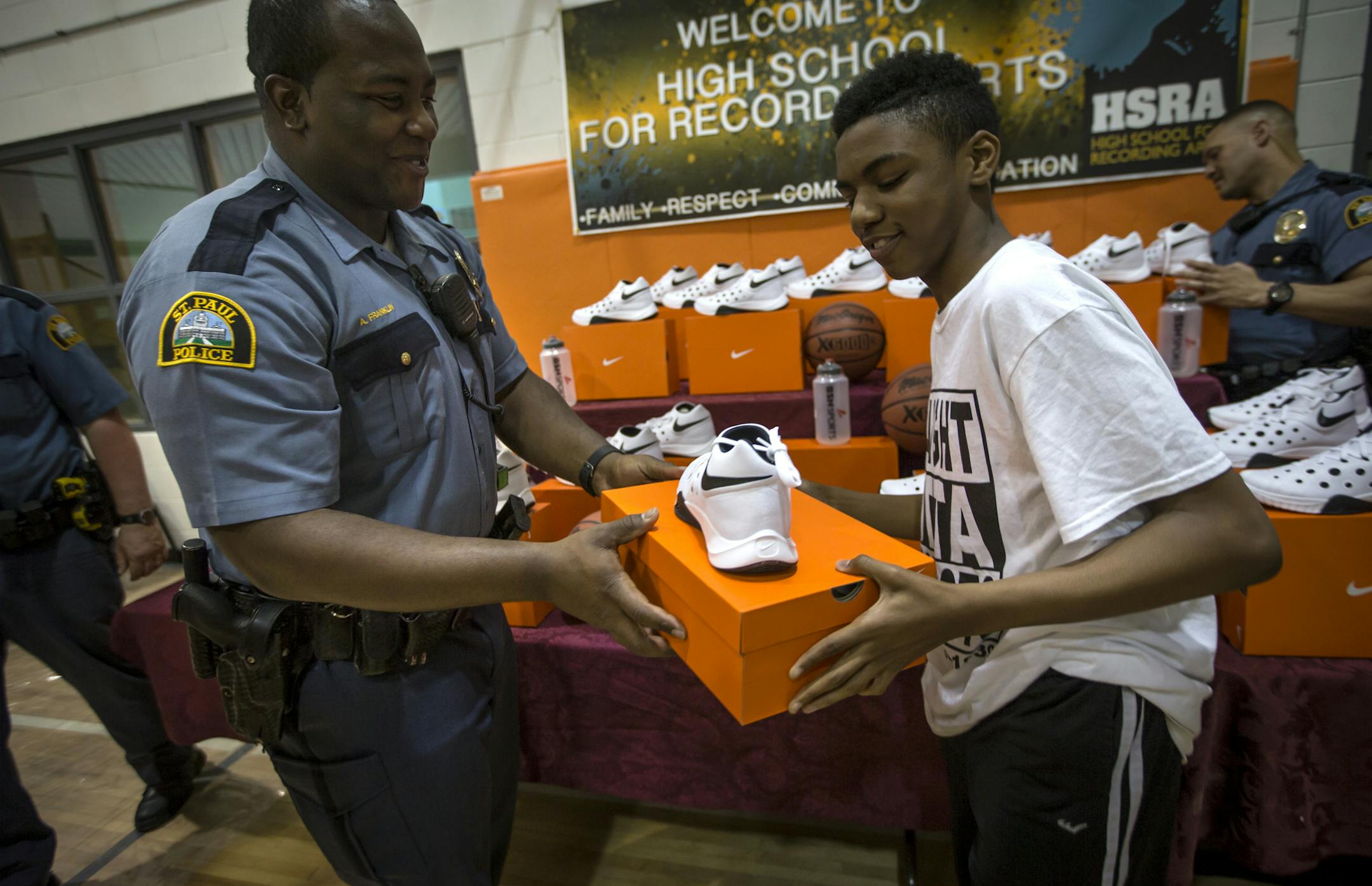 St. Paul police officer Andrew Franklin handed Norman Strickland a pair of sneakers at High School for Recording Arts in St. Paul, Minn. on Wednesday, April 20, 2016. ] RENEE JONES SCHNEIDER * reneejones@startribune.com St. Paul cop Tom Reis noticed kids at a school where he worked off-duty were playing basketball in street shoes. He raised money to buy them basketball sneakers and handed them out with other cops Wednesday at High School for Recording Arts.