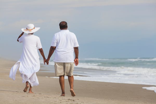 Happy romantic senior African American man and woman couple walking holding hands on a deserted tropical beach
