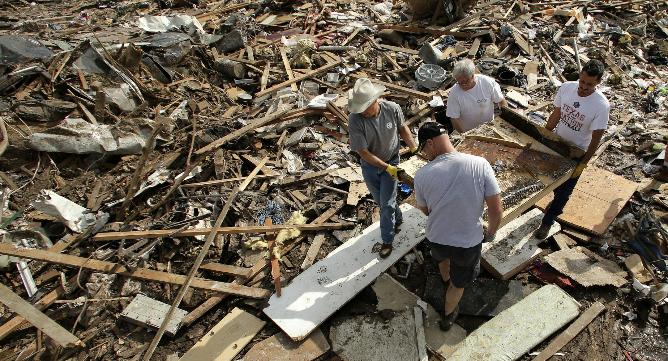 FILE - In this May 25, 2013 file photo, friends and family members carry what remains of piano through the rubble at a tornado-ravaged home, in Moore, Okla. Before construction workers can begin rebuilding the town of Moore, they have to overcome a mile-high pile of crushed wood, shattered glass, obliterated belongings and squished siding. (AP Photo/Charlie Riedel, File)