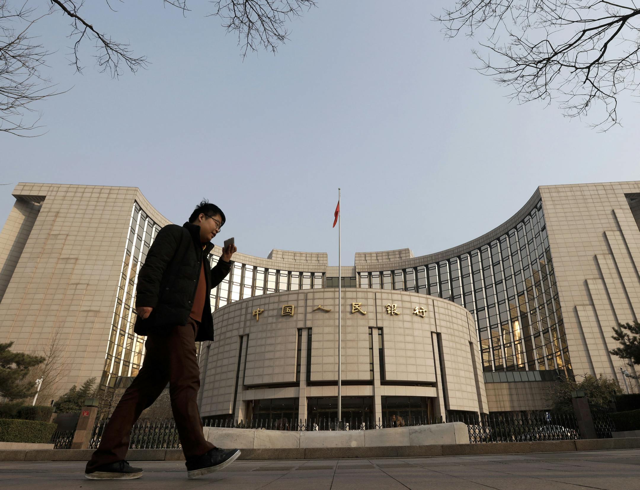 A man walks past China's central bank, or the People's Bank of China, in Beijing, Sunday, March 10, 2019. China's central bank governor Yi Gang says American and Chinese envoys discussed sticking to promises to avoid currency devaluations to boost exports during negotiations aimed at ending a tariff war. (AP Photo/Andy Wong) ORG XMIT: XAW108