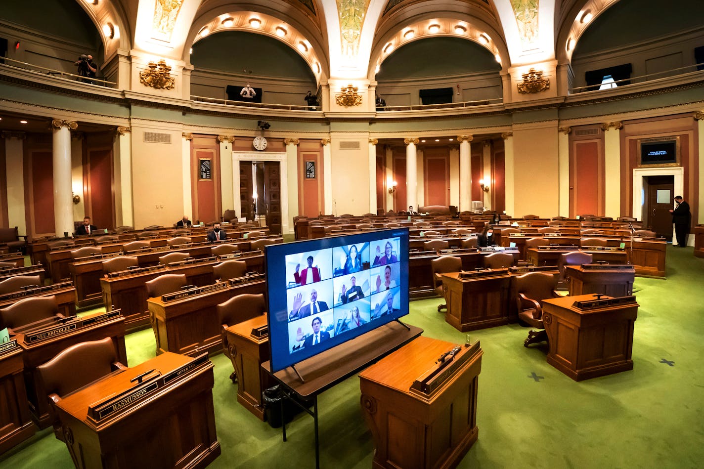 Legislatures are displayed on a monitor as they are sworn-remotely in groups of nine in the nearly-empty House Chamber at the Minnesota State Capitol, Tuesday, Jan. 5, 2021, in St. Paul, Minn. A few took the oath in person earlier. (Glen Stubbe/Star Tribune via AP)