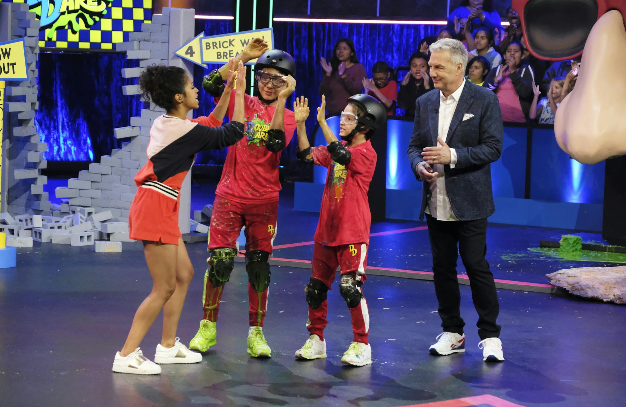 This undated image released by Nickelodeon shows Liza Koshy left, and Marc Summers, right, with contestants on the game show "Double Dare," in Los Angeles. Nickelodeon is joining with HQ Trivia to celebrate the "Double Dare" reboot. A 1990s-themed trivia game will pair the Nickelodeon show's original host, Marc Summers, with HQ host Scott Rogowsky. (Trae Patton/Nickelodeon via AP)
