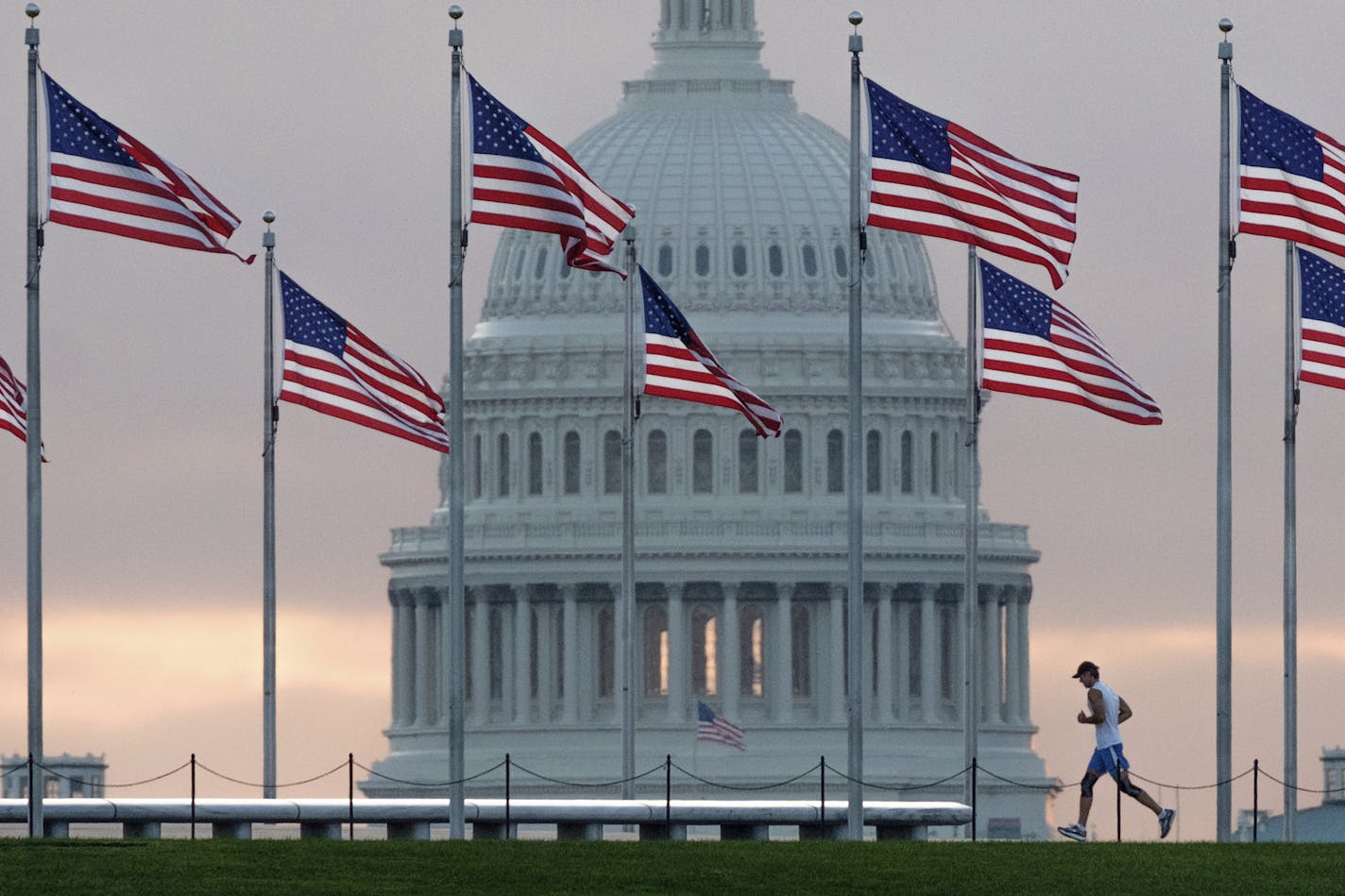 FILE - In this Sept. 27, 2017, file photo, a early morning runner crosses in front of the U.S. Capitol as he passes the flags circling the Washington Monument in Washington. With passage of an enormous budget bill, Congress has all but wrapped up its legislating for the year _ in March. Now lawmakers have to run on what they&#x2019;ve got: a tax cut bill, big spending increases and no fixes to immigration. (AP Photo/J. David Ake, File)