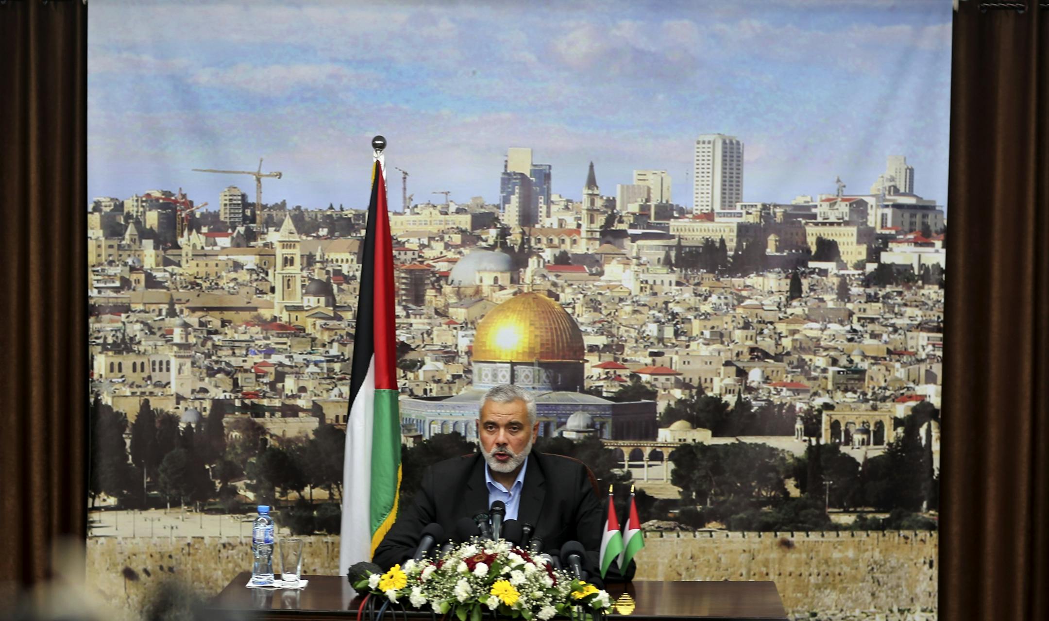 Ismail Haniyeh, the outgoing Hamas prime minister in Gaza, speaks in front of a banner that shows Jerusalem, at his office in Gaza City, Monday, June 2, 2014. President Mahmoud Abbas on Monday swore in a Palestinian unity government, taking a major step toward ending a crippling territorial and political split among the Palestinians but also setting the stage for new friction with Israel. And while none of the Cabinet members are believed to be affiliated with Hamas, it remains unclear if the U.