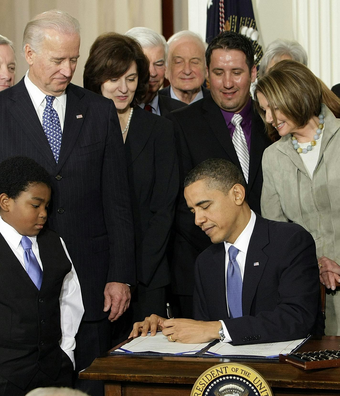 FILE - In this March 23, 2010 file photo, Marcelas Owens of Seattle, left, Rep. John Dingell, D-Mich., right, and others, look on as President Barack Obama signs the health care bill in the East Room of the White House in Washington. (AP Photo/J. Scott Applewhite, File)