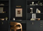An office painted in soft black with dark gray built-in bookcases with gold handles and a tan leather chair.