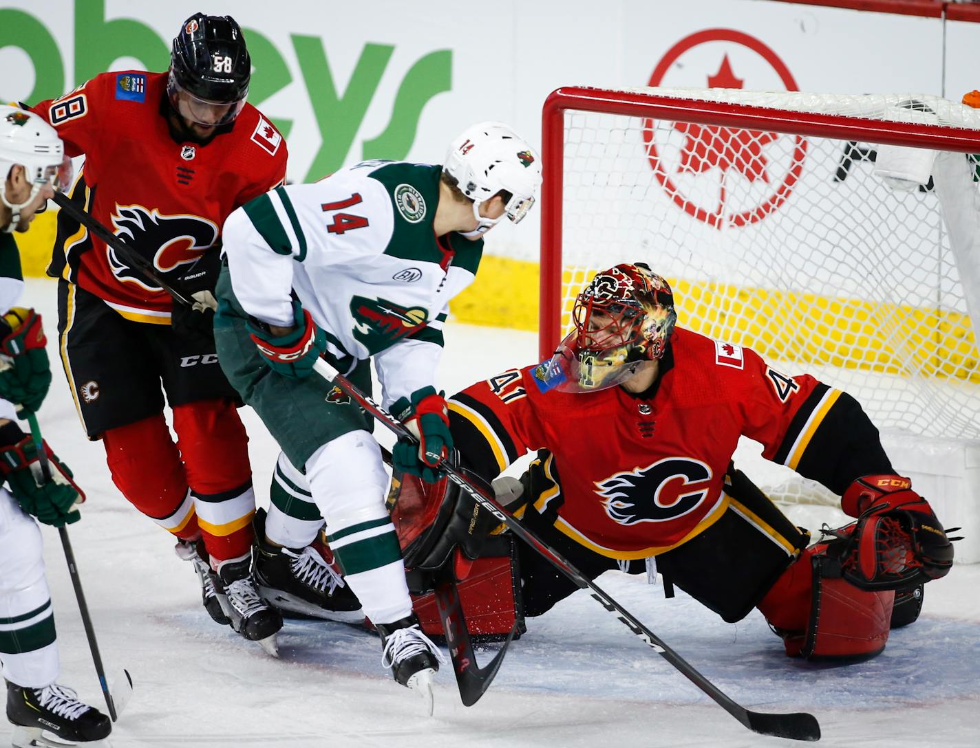 The Wild's Joel Eriksson, center, is shoved away from the net by Calgary Flames goalie Mike Smith as Oliver Kylington looks on