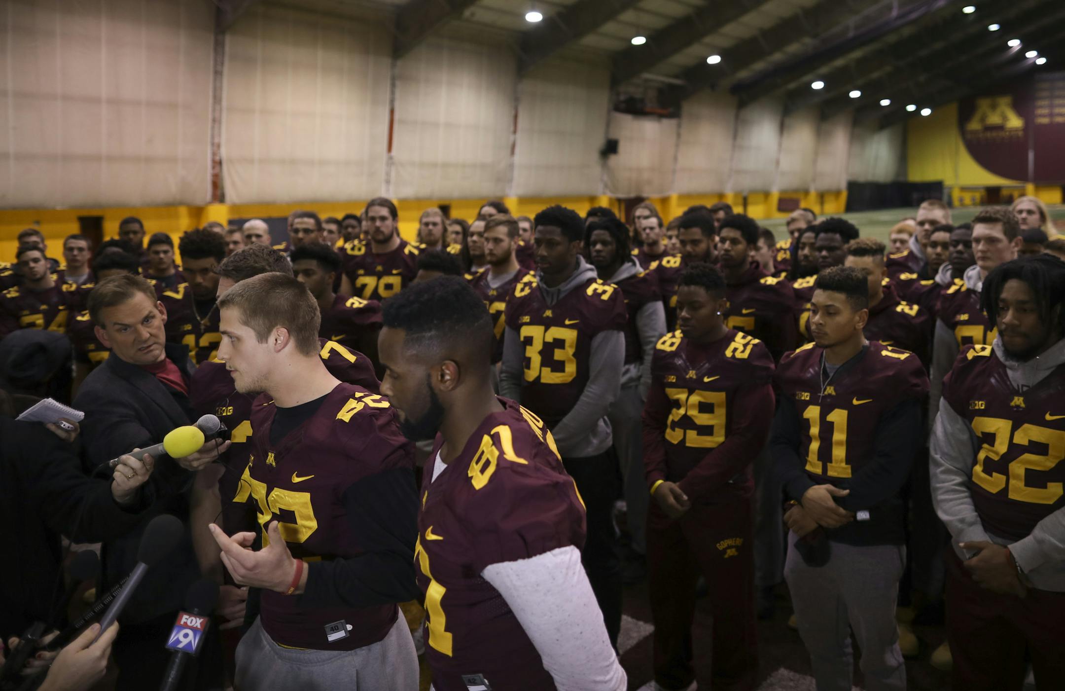 University of Minnesota wide receiver Drew Wolitarsky, flanked by quarterback Mitch Leidner, obscured behind Wolitarsky, and tight end Duke Anyanwu gestures as he stands in front of other team members while talking to reporters in the Nagurski Football Complex in Minneapolis, Minn., Thursday night, Dec. 15, 2016. The players delivered a defiant rebuke of the university's decision to suspend 10 of their teammates, saying they would not participate in any football activities until the school presi