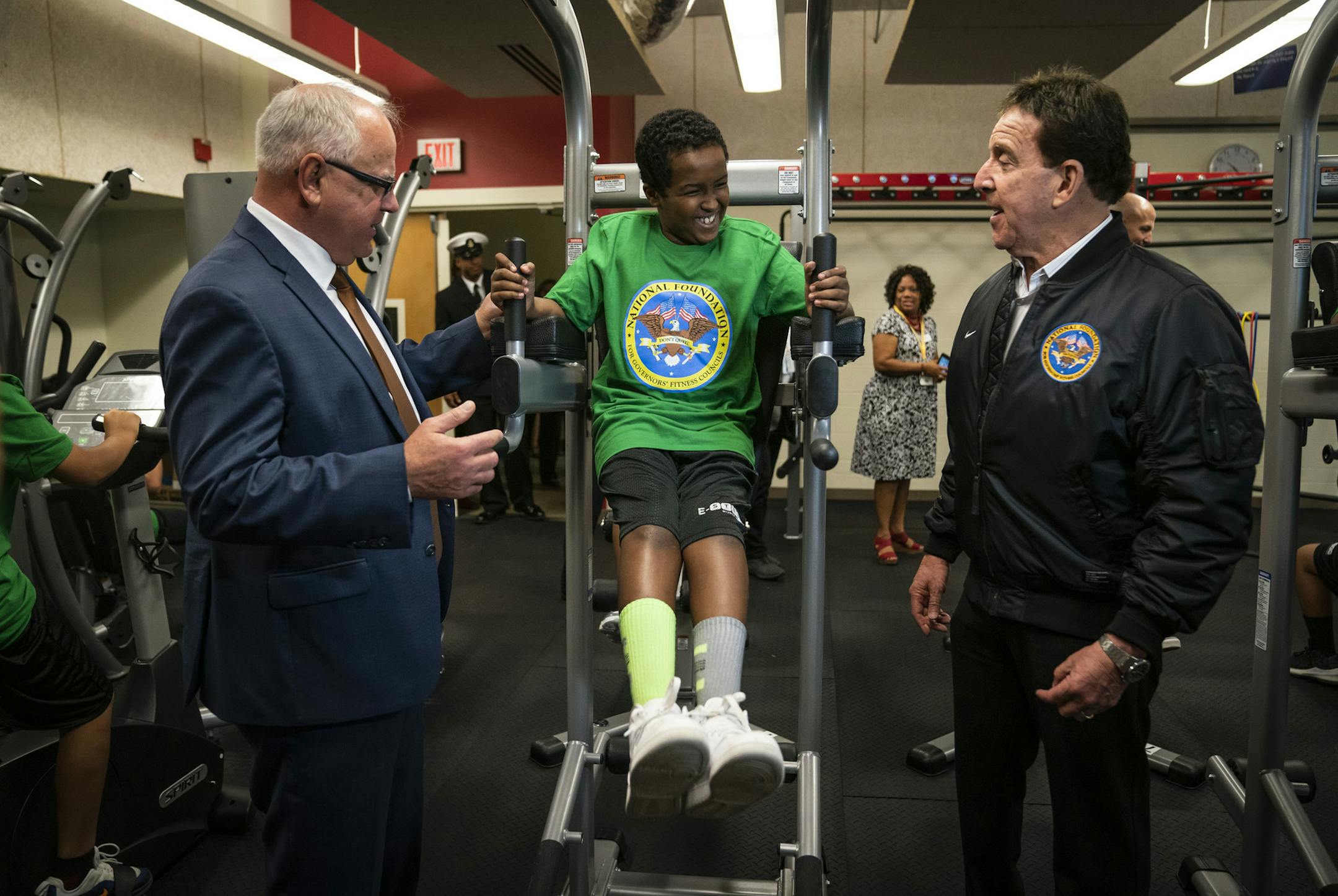 Gov. Tim Walz, left, and actor and fitness trainer Jake Steinfeld chatted with student Yusuf Ali as he tried out E-STEM Middle School's new fitness center.