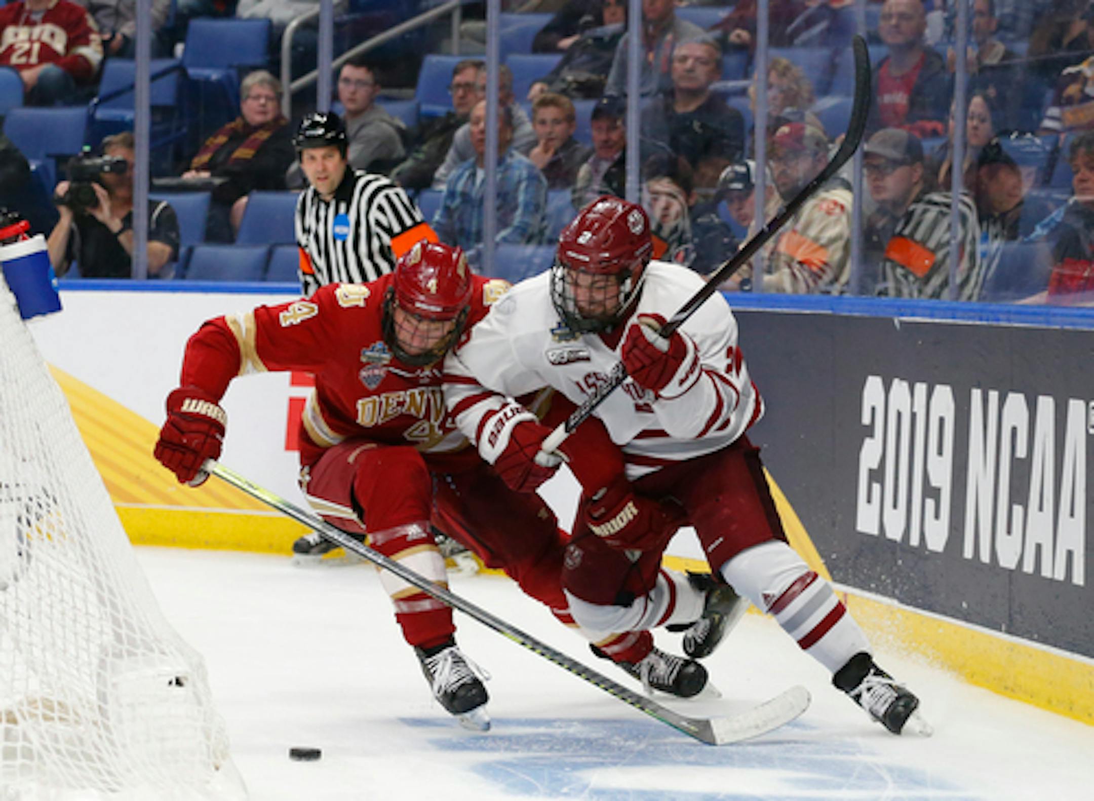 Massachusetts defenseman Marc Del Gaizo (2) and Denver defenseman Griffin Mendel (4) race to the puck behind the net during the third period in a semifinal of the Frozen Four NCAA men's college hockey tournament Thursday, April 11, 2019, in Buffalo, N.Y. (AP Photo/Jeffrey T. Barnes)