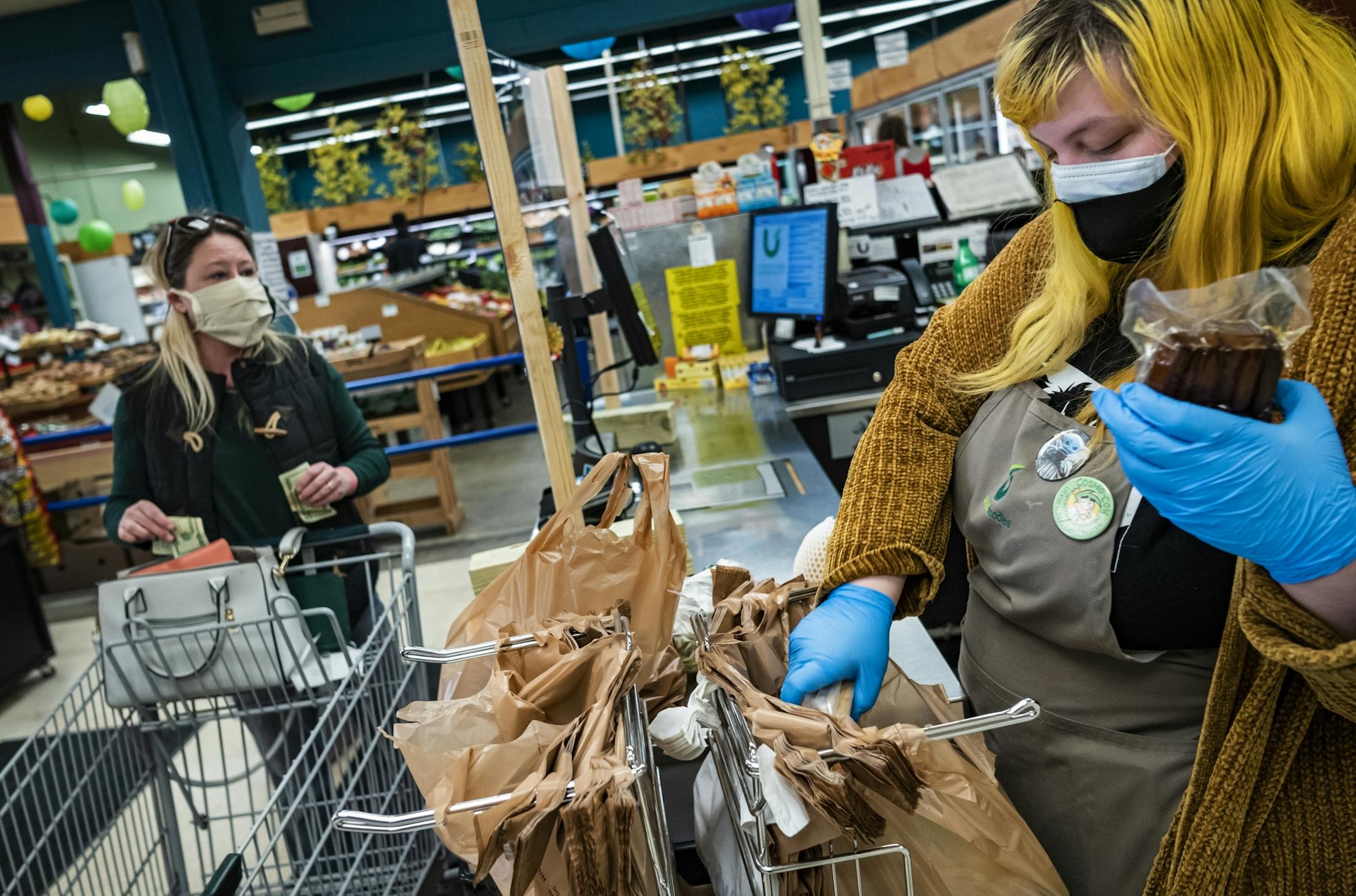 Checkout clerk Kaillie Reeves works behind a protective screen something she suggested her employer implement at a weekly committee meeting held to improve working conditions. Customer Amy hart wears a a mask made by her mother.