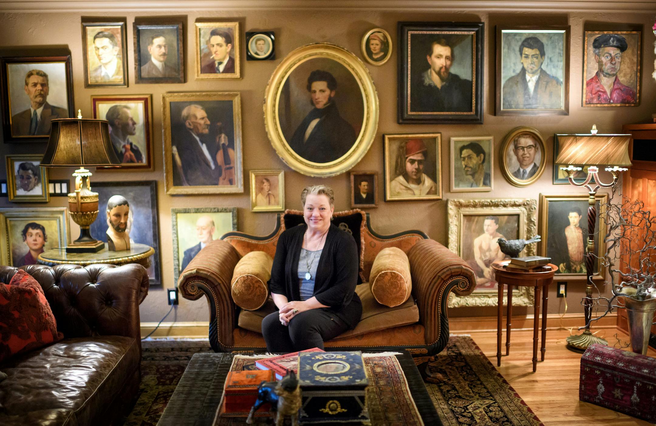 Tina Wilcox posed in her family room, in front of her “man wall,” which is covered with vintage male portraits. Her home is filled with artifacts she’s collected from all over the world.